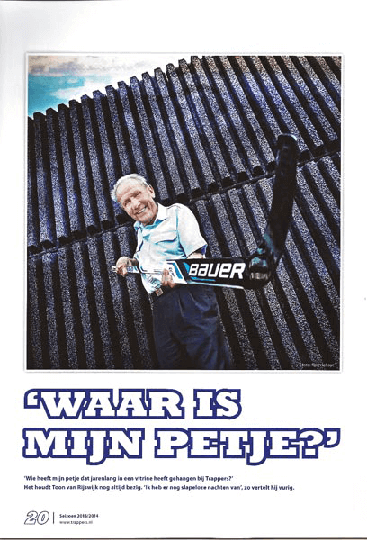 Jongen met een pack ice hockey sticks die een poster vasthoudt met de tekst 'Waar is mijn petje?' en een achtergrond met een scheidingshek.