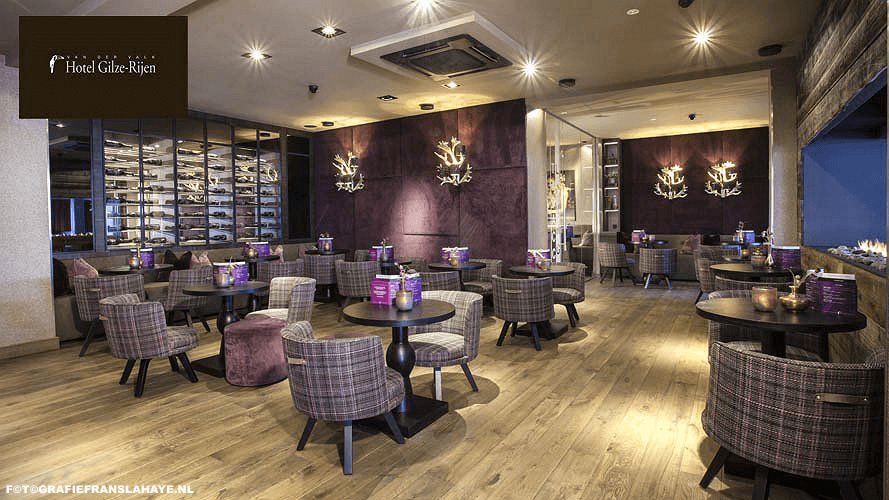 Een elegant restaurant met ronde tafels en plaid fauteuils, decoratieve wandlichten en een wijnrek aan de muur, met een warme sfeer.