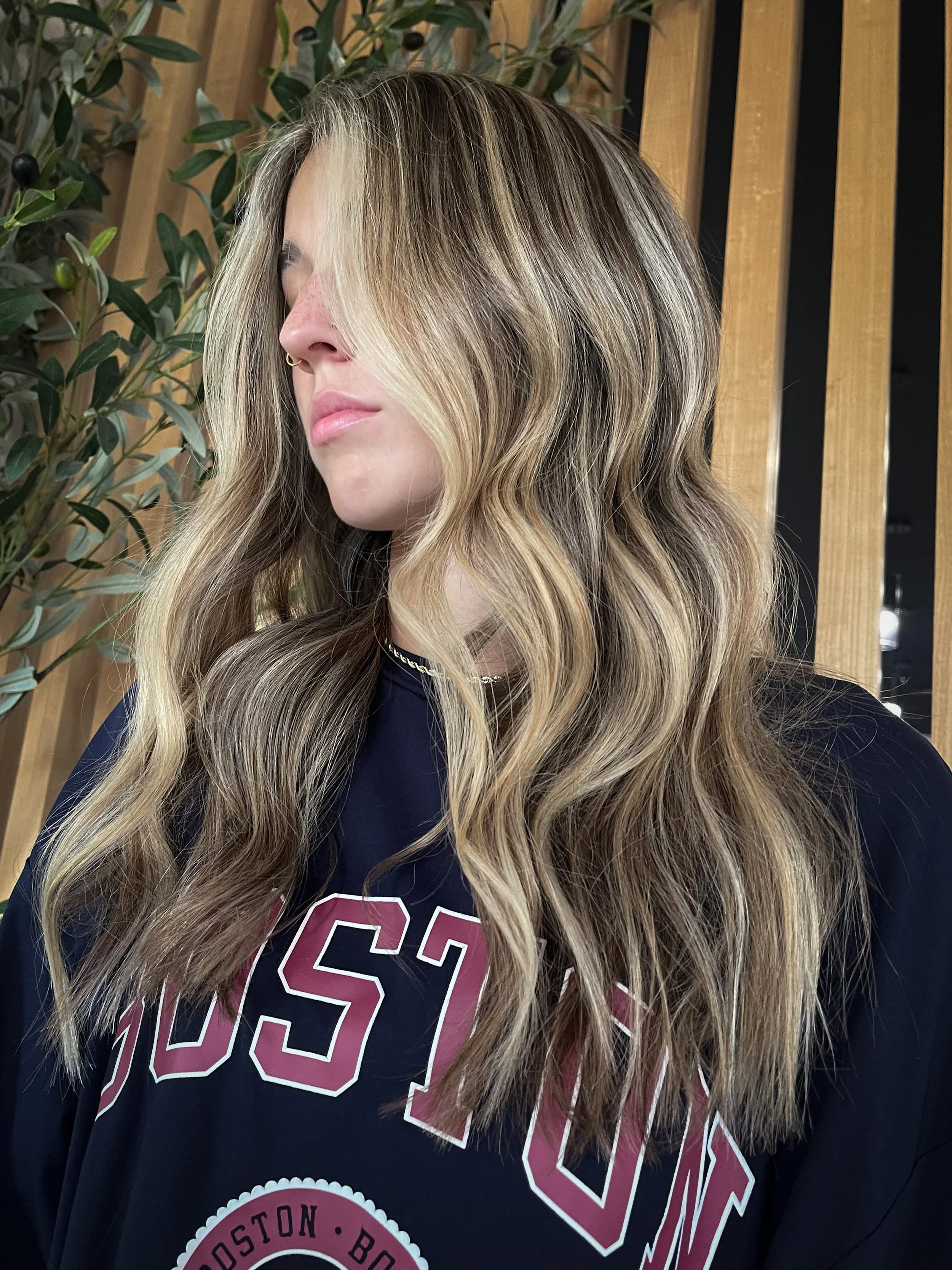 Woman posing while showing off her brunette hair with her lived in blonde highlights. 