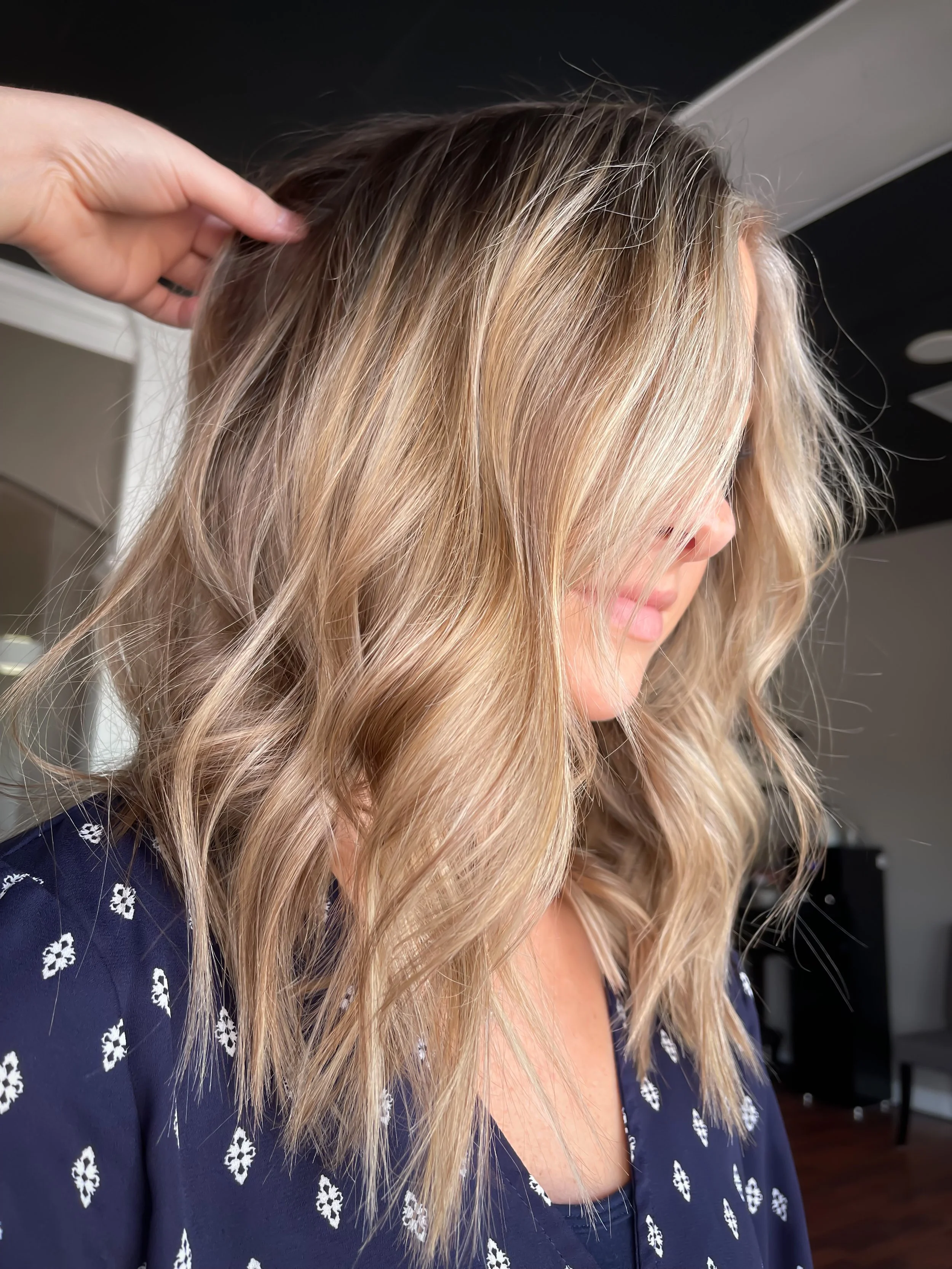 Close-up of a woman with shoulder-length, wavy blonde hair, wearing a navy blue top with white floral patterns.