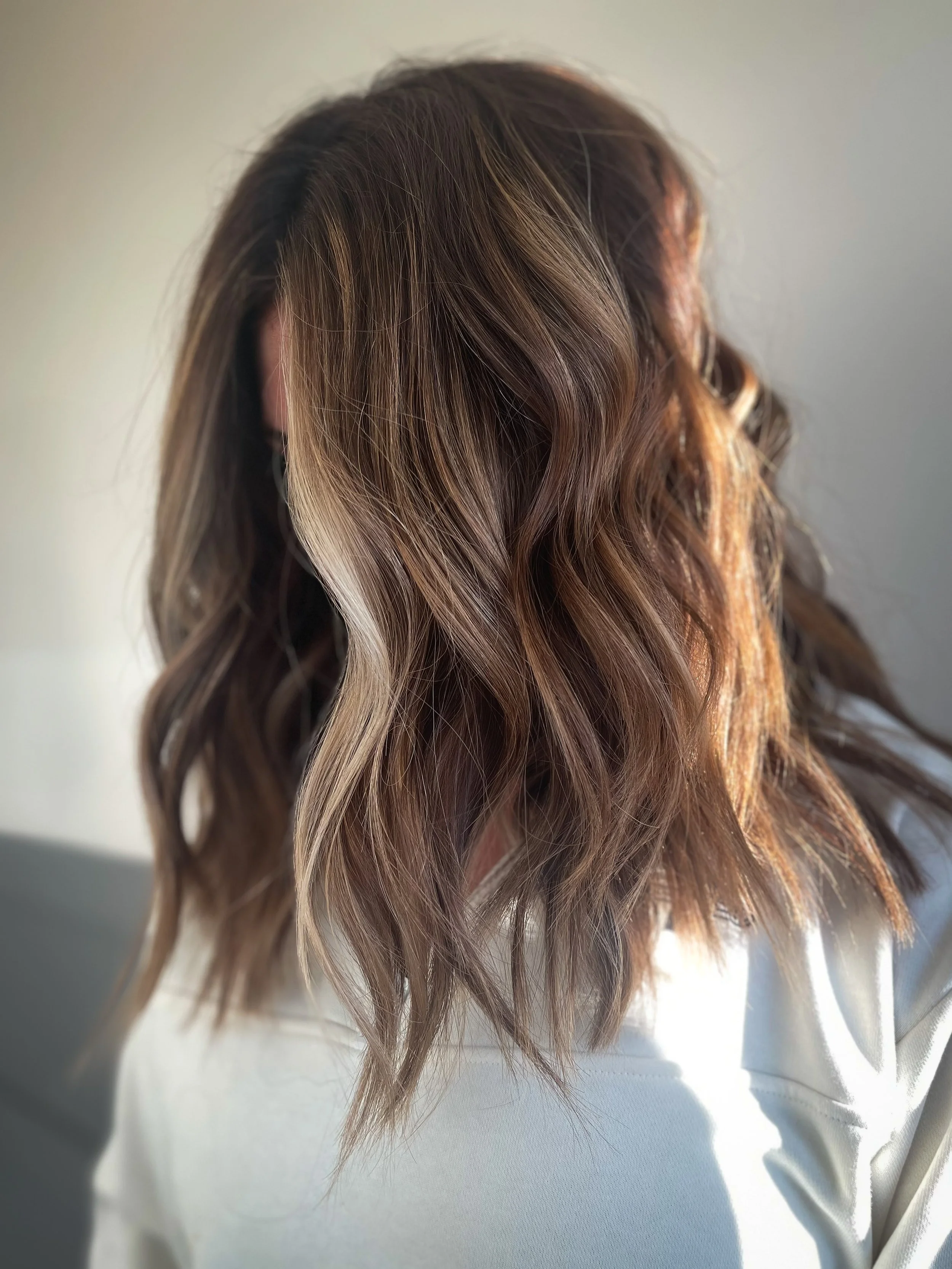 Close-up of a woman's hair styled in loose waves, with a balayage effect blending dark brown and light blonde highlights.