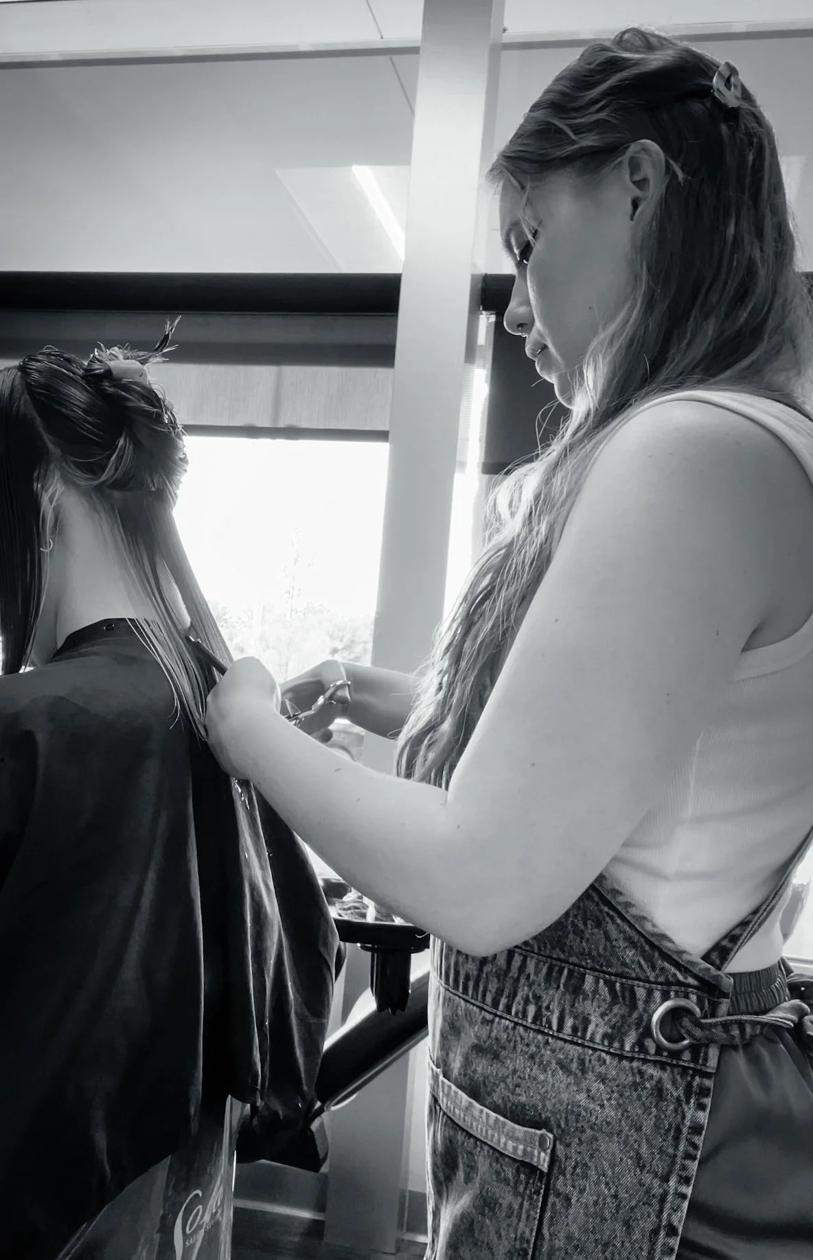 A woman with long hair is getting her hair cut by a hairstylist in a salon. The photo is in black and white.