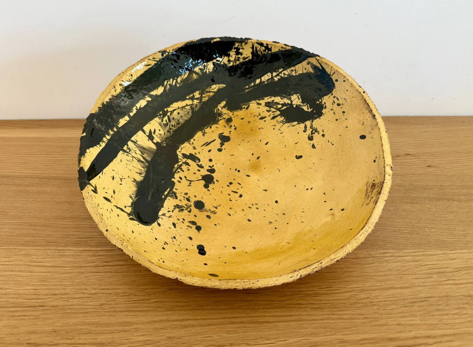 Large honey glazed bowl with bold splatter decoration in black on a wooden surface