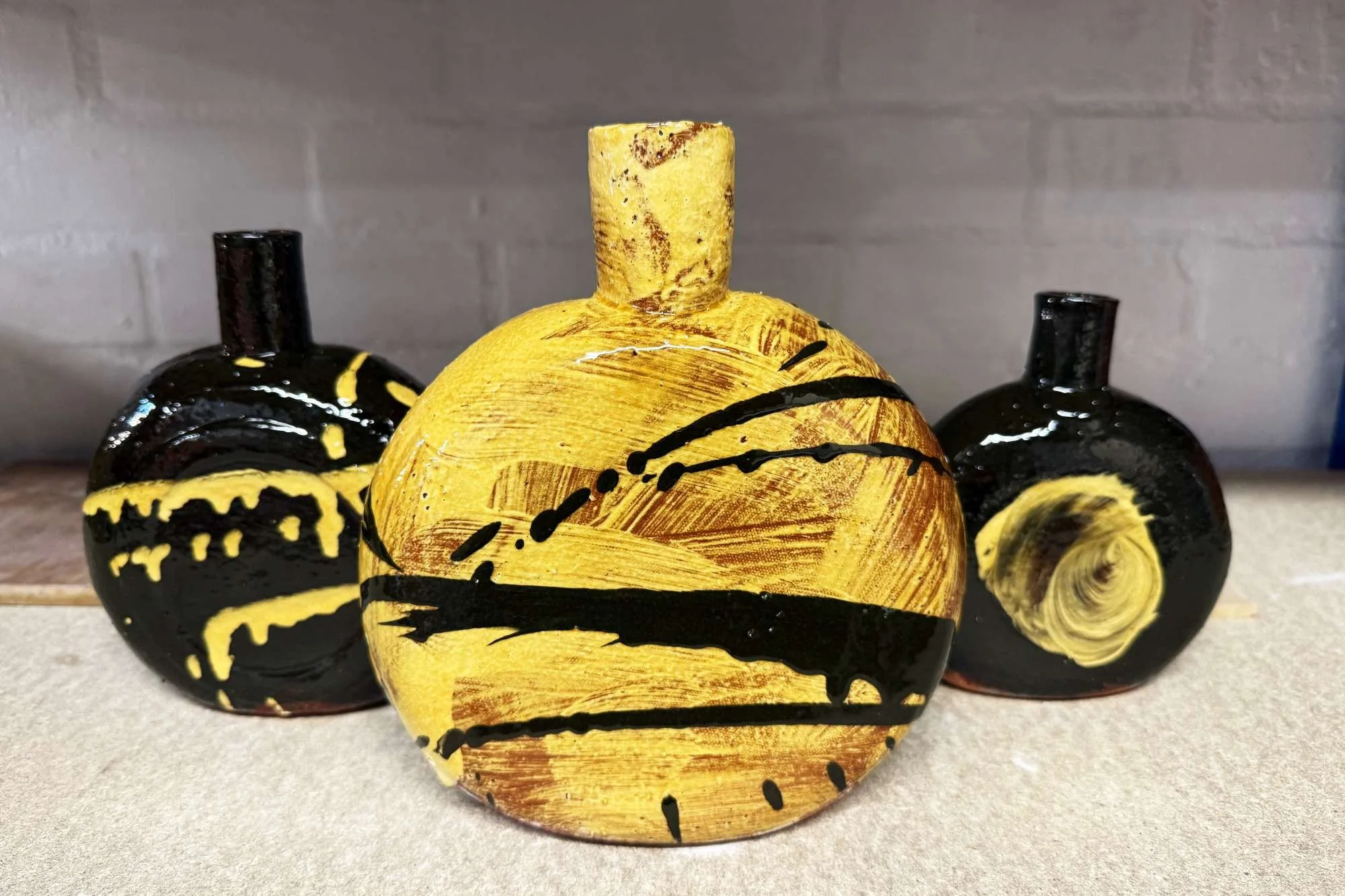 Three decorative pumpkins with black and yellow paint designs on a beige surface against a gray wall.