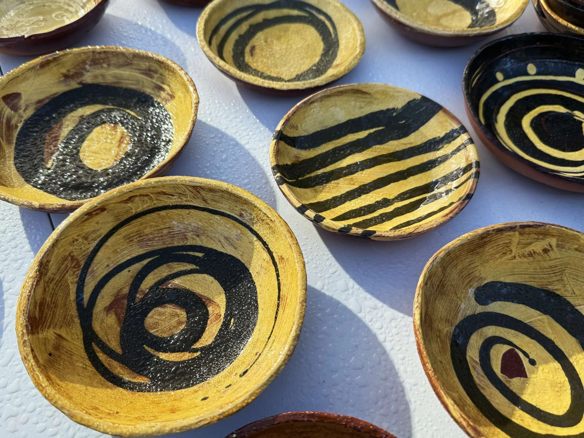 Colorful ceramic bowls with black and yellow swirl and stripe patterns on a white surface.