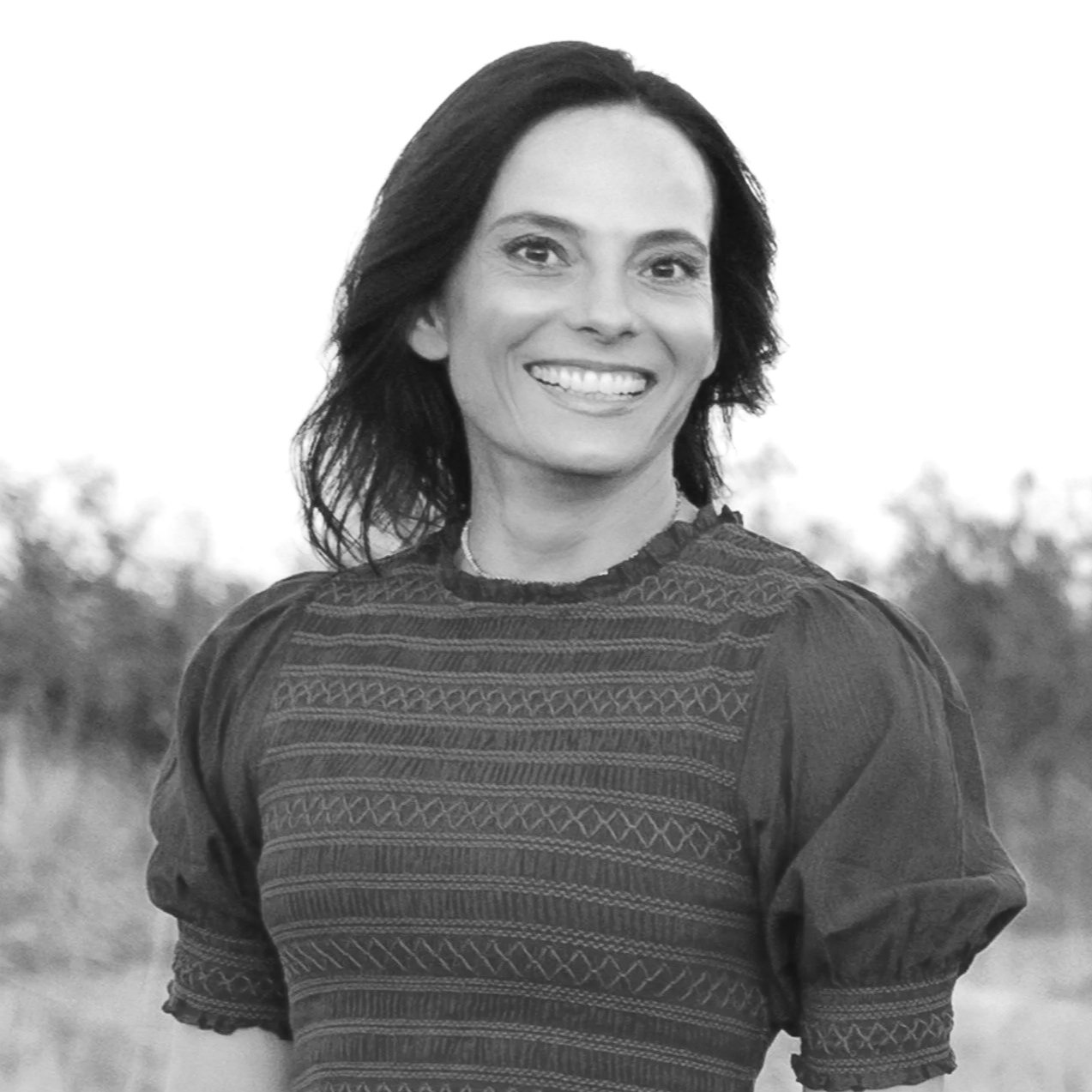 Black and white photo of a woman smiling outdoors, wearing a patterned dress with puffed sleeves.