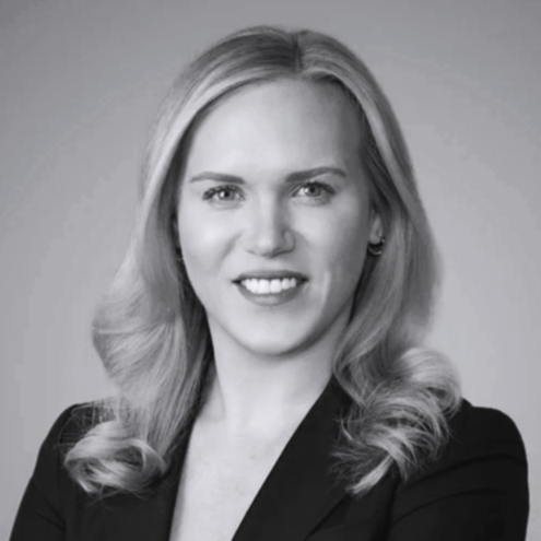 Black and white professional portrait of a woman with wavy blonde hair, wearing a blazer, smiling at the camera.