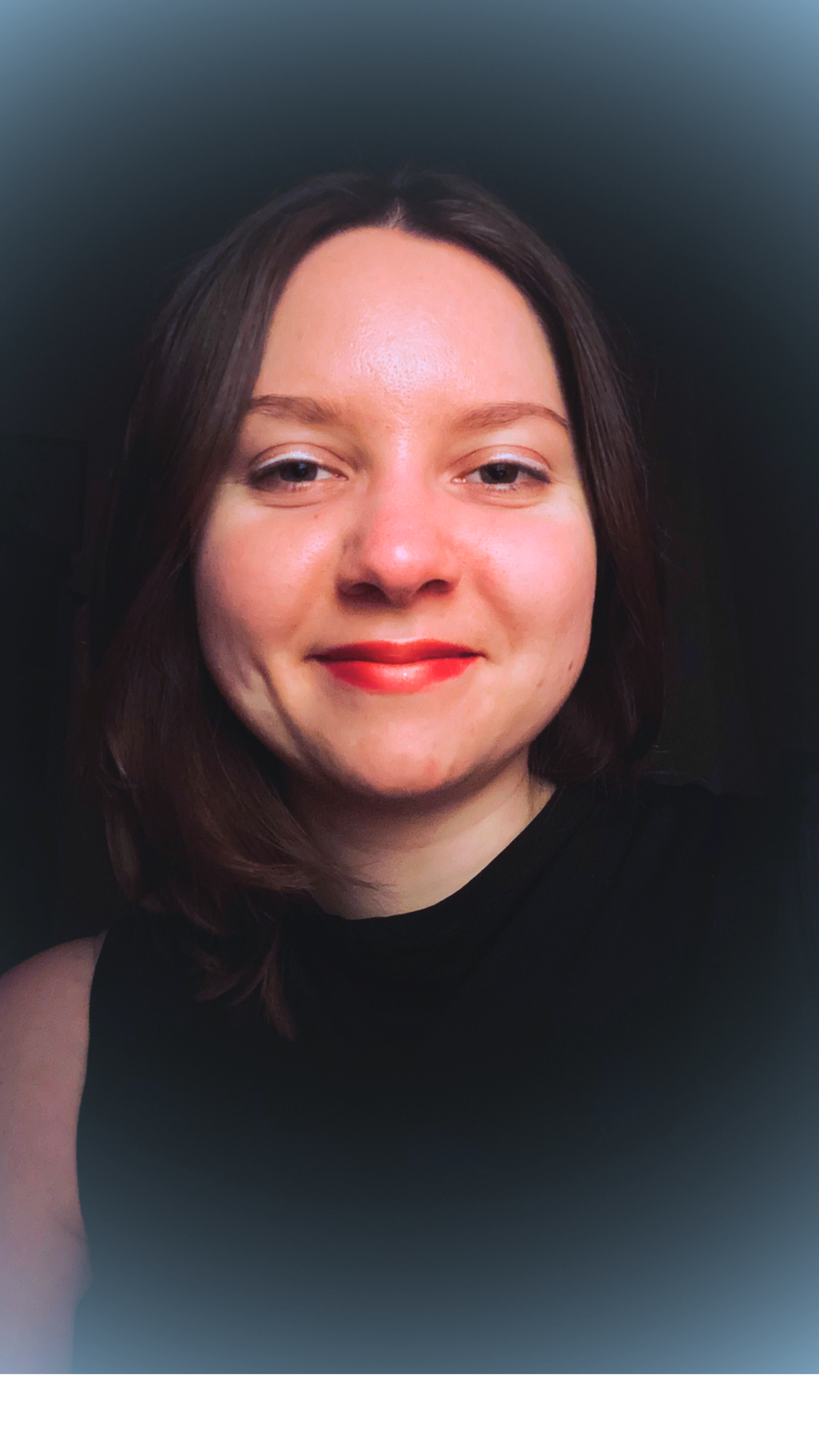 Nahaufnahme eines lachenden jungen Mädchens mit braunen Haaren, rotem Lippenstift und schwarzen Oberteil.