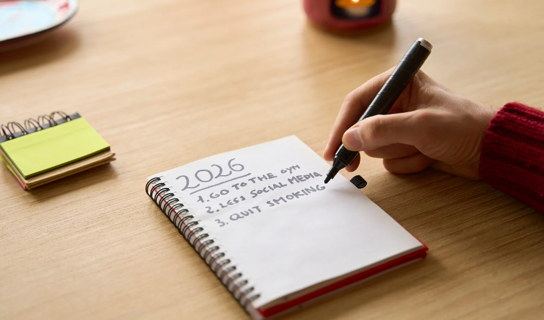 A hand with a black pen writing out new years resolutions in a list for 2026