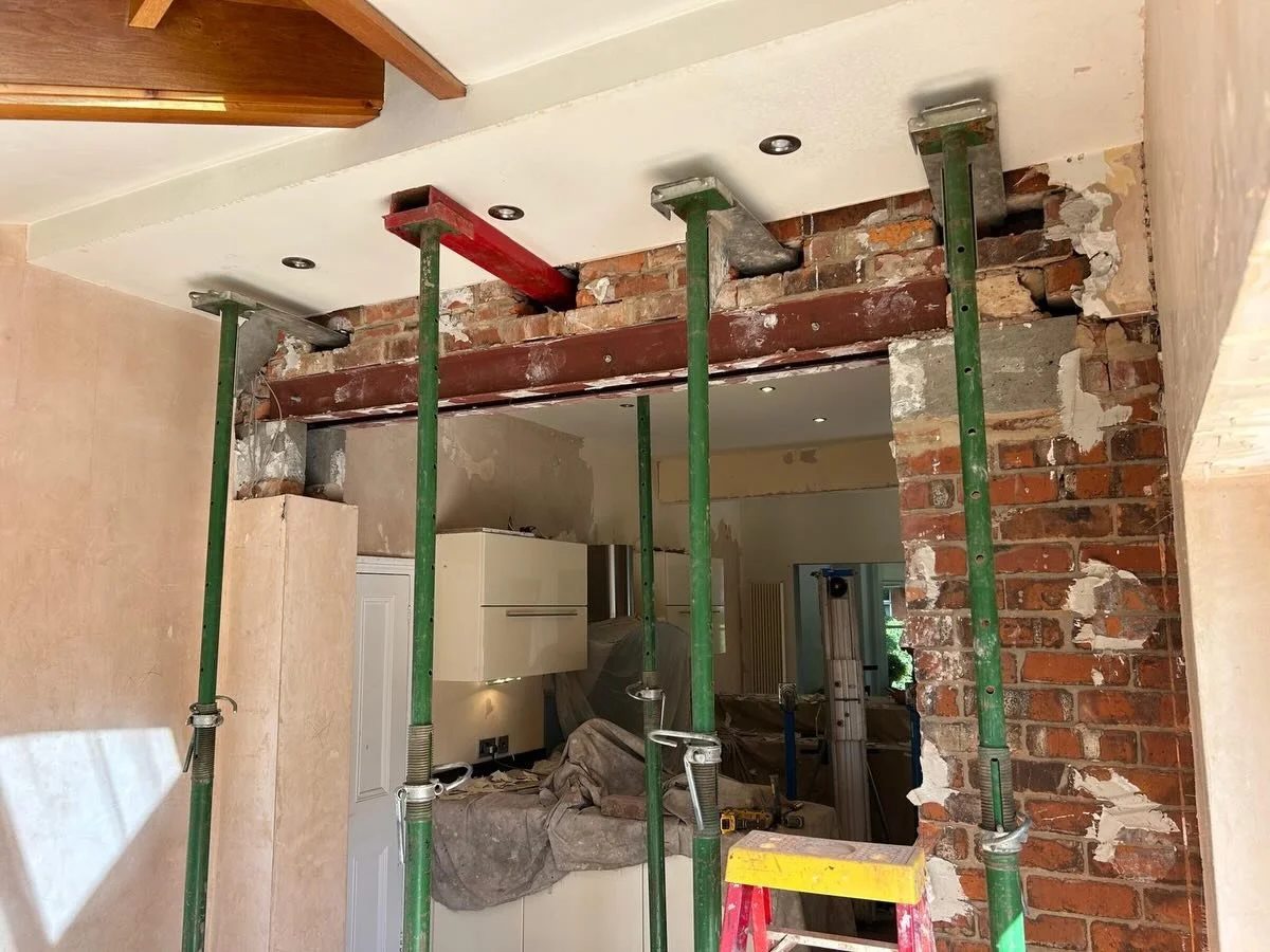 Interior renovation with exposed brick wall, green supporting scaffolding, construction tools, and partially finished drywall ceiling.