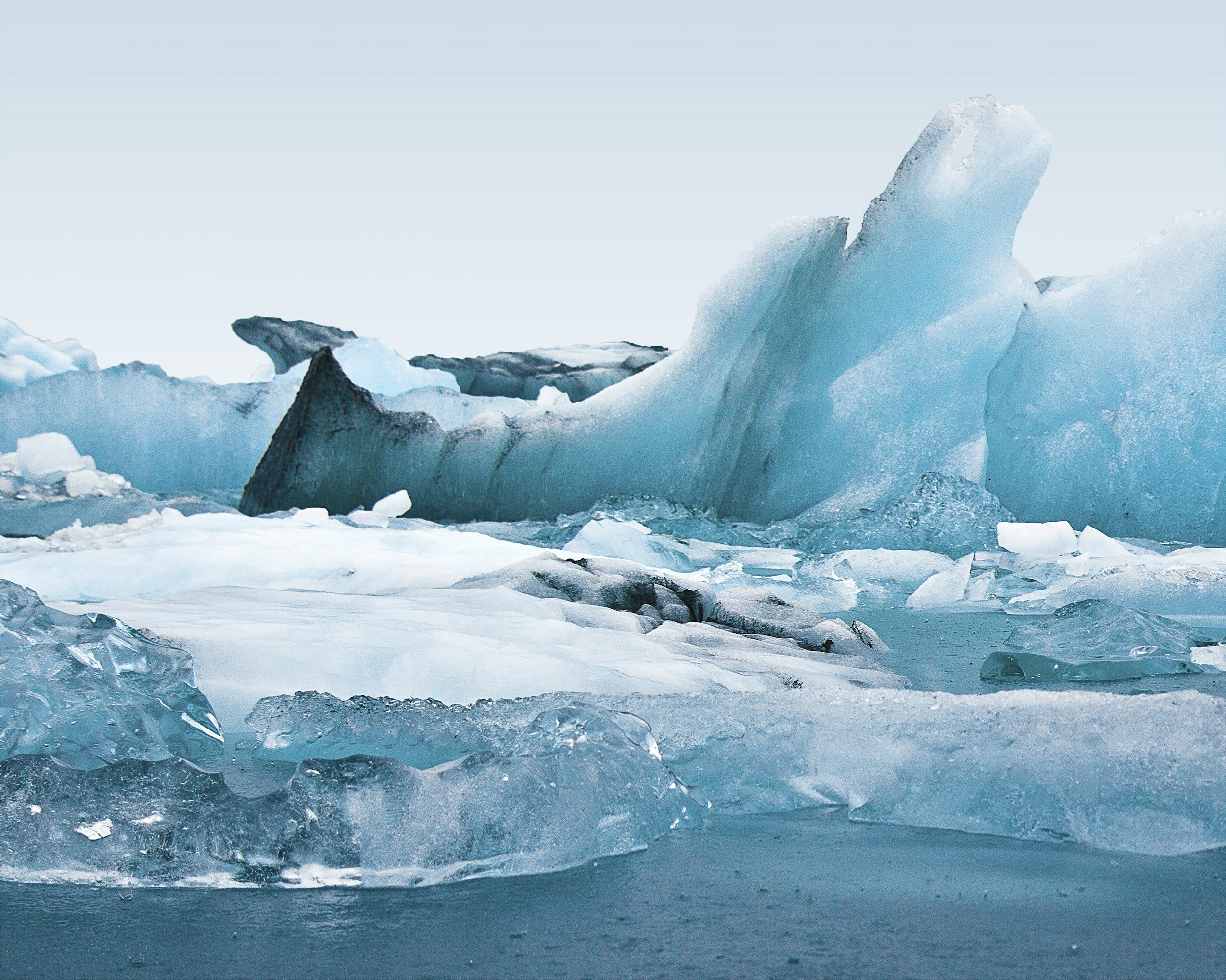Icebergs floating in a cold, icy ocean, with one prominent large iceberg with a sharp peak.