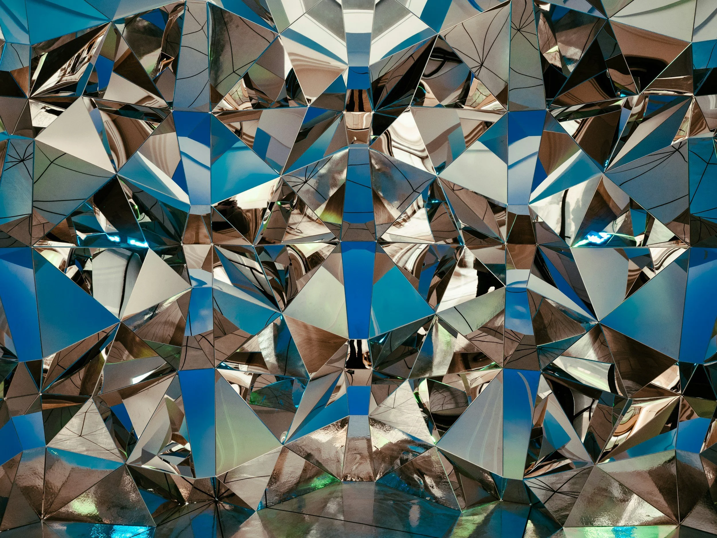 A reflective, geometric sculpture made up of many triangular mirrored facets.