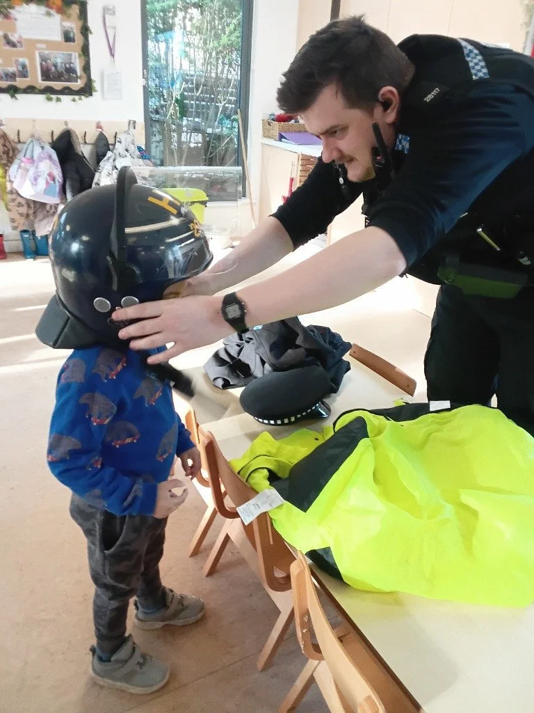 A toddler trying on a policeman's helmet during a visit by the local police