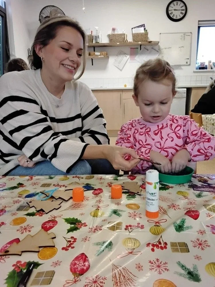 Parent and child working together on a crafts activity during nursery parent day, seated at a table