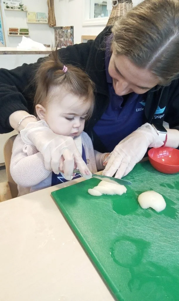 A young girl cutting some dough with assistance from a nursery practitioner
