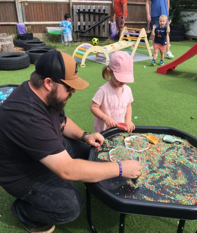 A young girl playing at a messy play tray with her Dad during a family day.