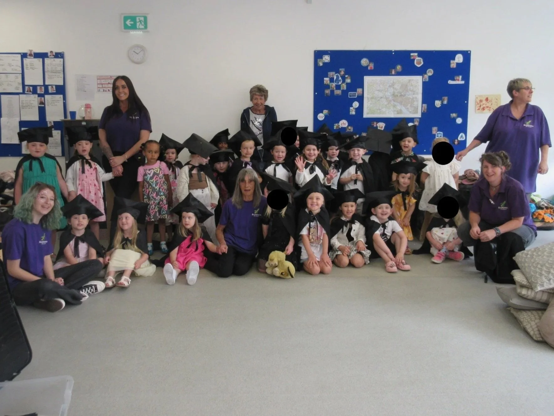 A group of young children in graduation caps and gowns with their teachers in a classroom.