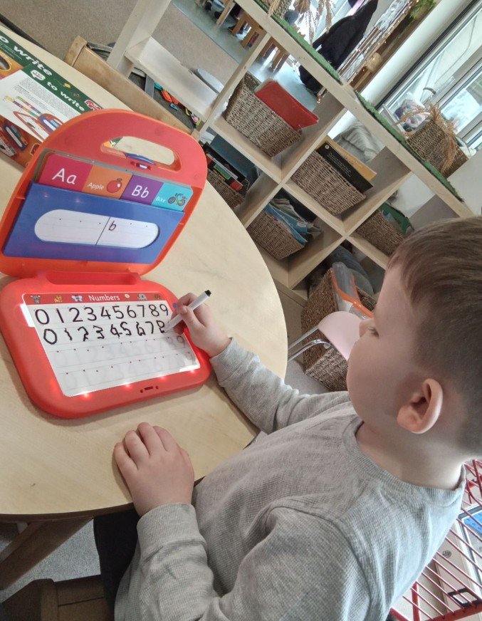 A young boy independently learning to write numbers using a whiteboard & marker toy