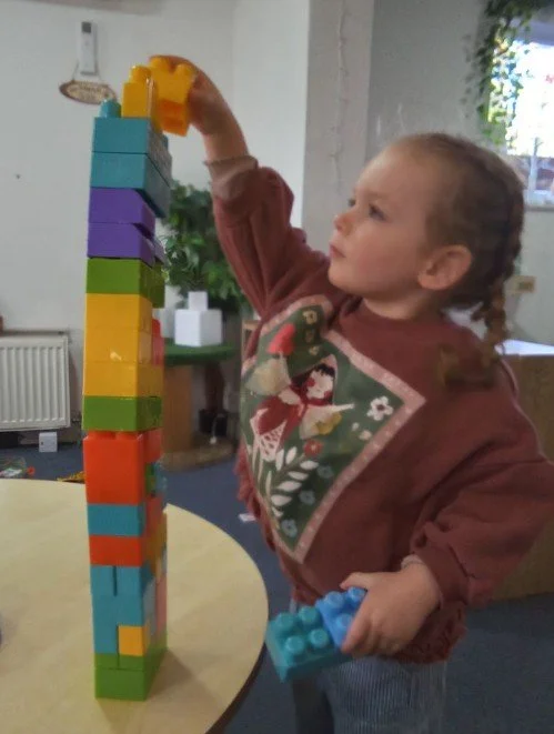 Young girl stacking colorful toy blocks into a tall tower at a table.