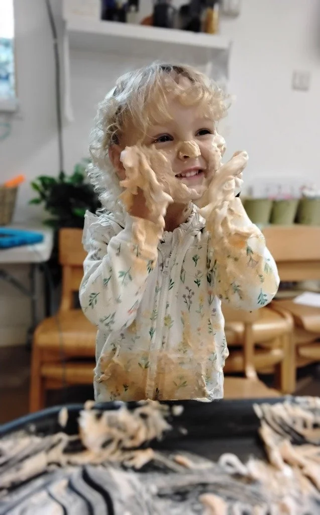 A toddler smiling & having fun during a messy play activity.