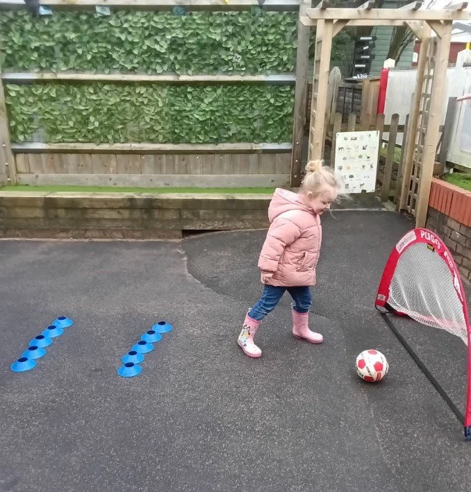 A young girl playing football outside during a visit from Little Kickers