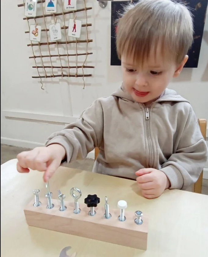 A young boy playing with a wooden block and various screws and bolts of different sizes and shapes