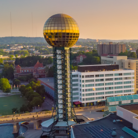 Landmark with a large metallic sphere atop a tall lattice tower in an urban area at sunset.