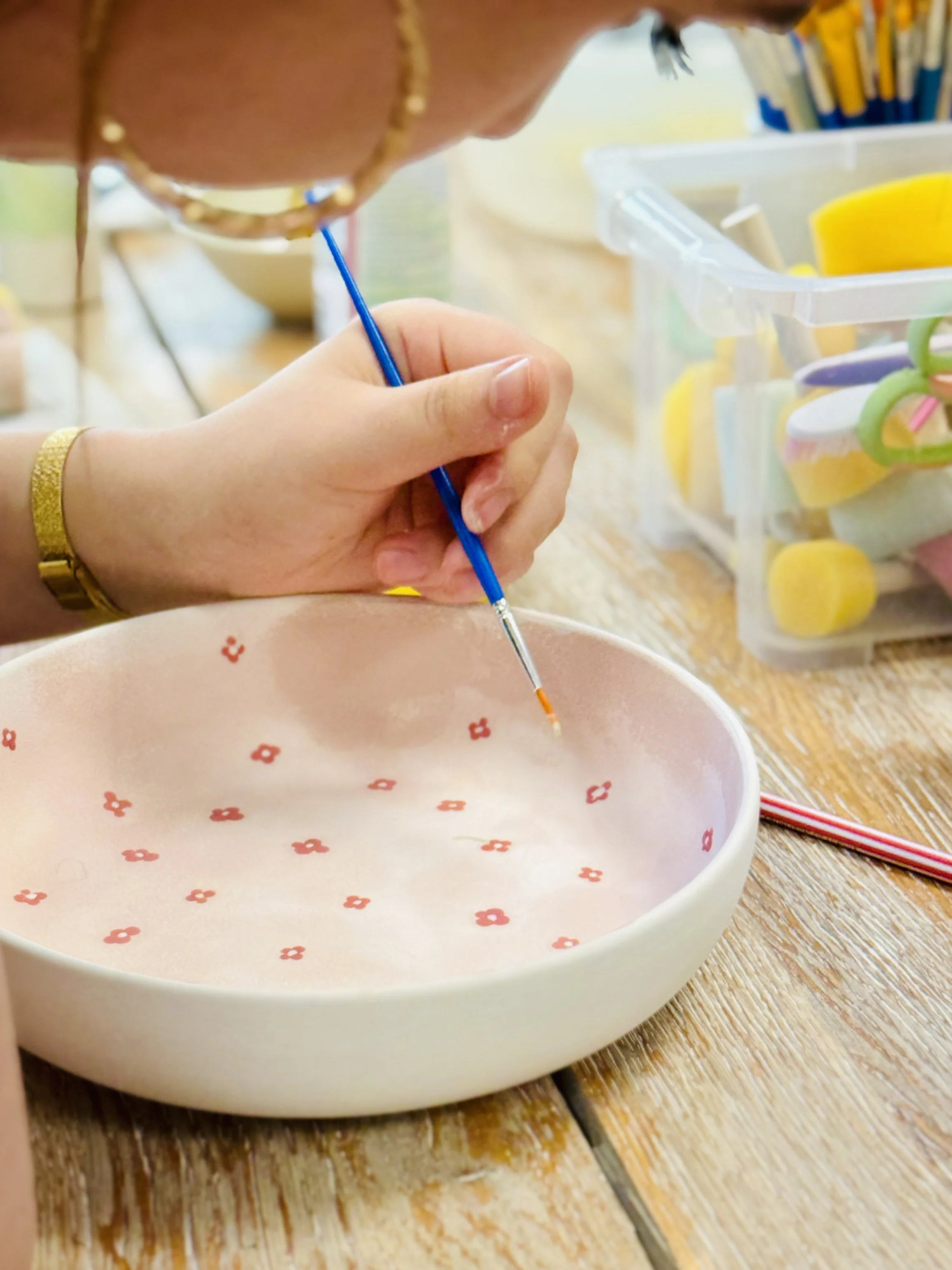 Une personne peignant un motif de petites fleurs rouges sur une assiette en céramique blanche.