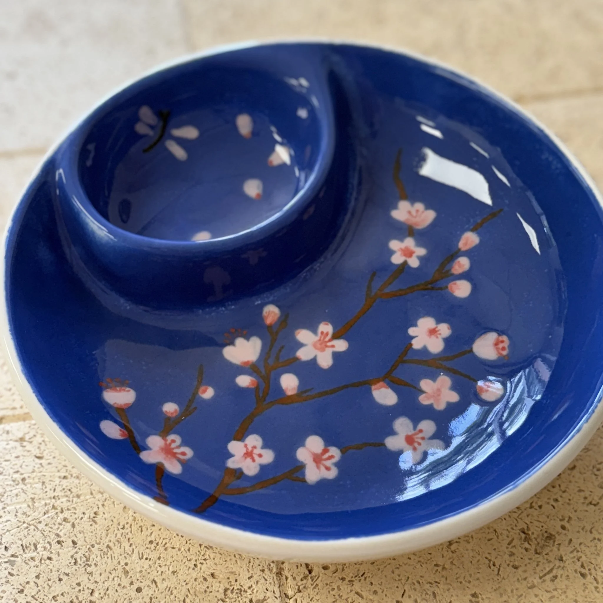 Assiette en céramique bleue avec un petit bol à l'intérieur, décorée de cerisiers en fleurs roses et branches marron.