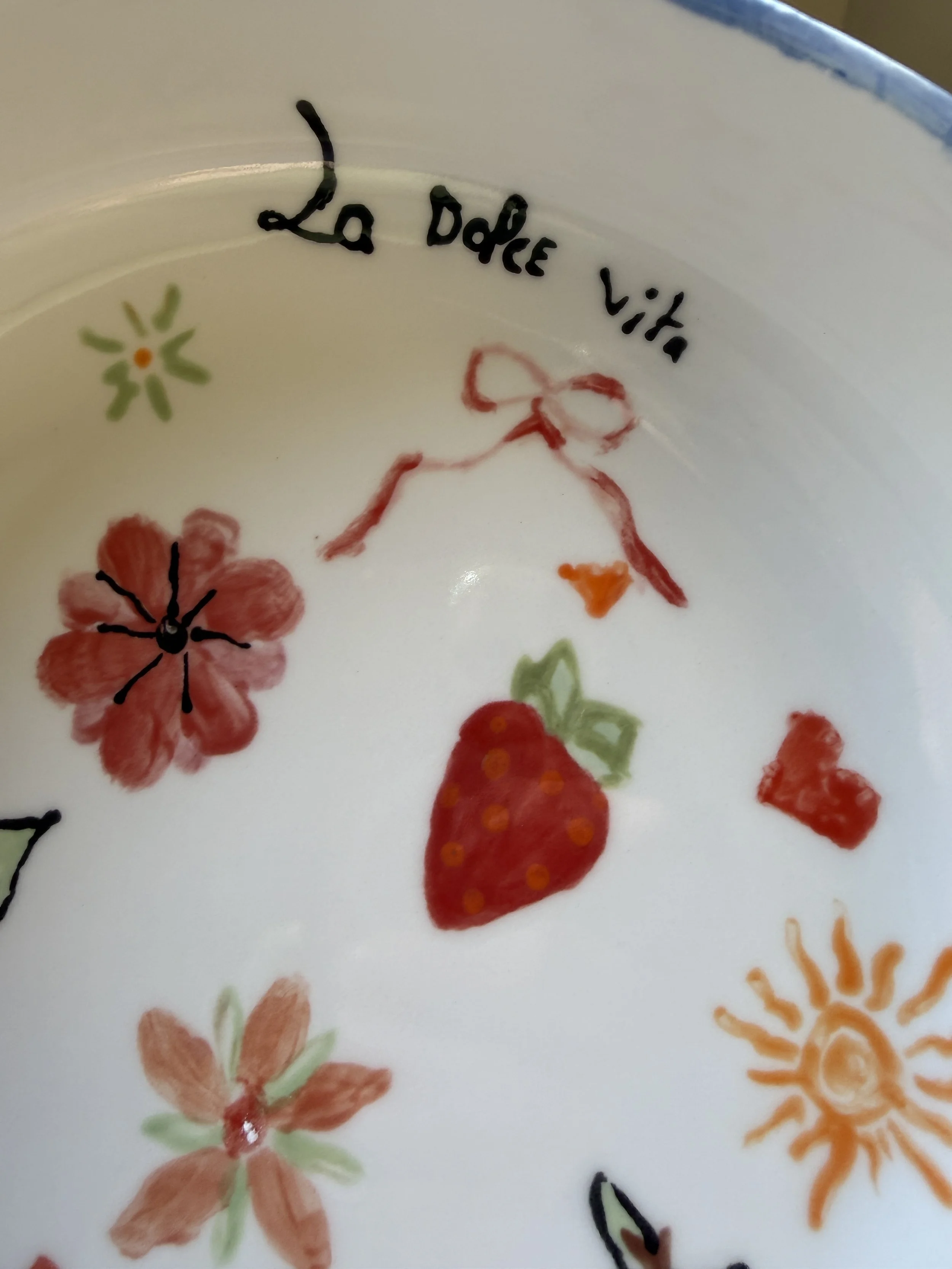 Un bol blanc avec des dessins de fruits, fleurs et soleil, et l'écriture en français 'La Dée vita'.