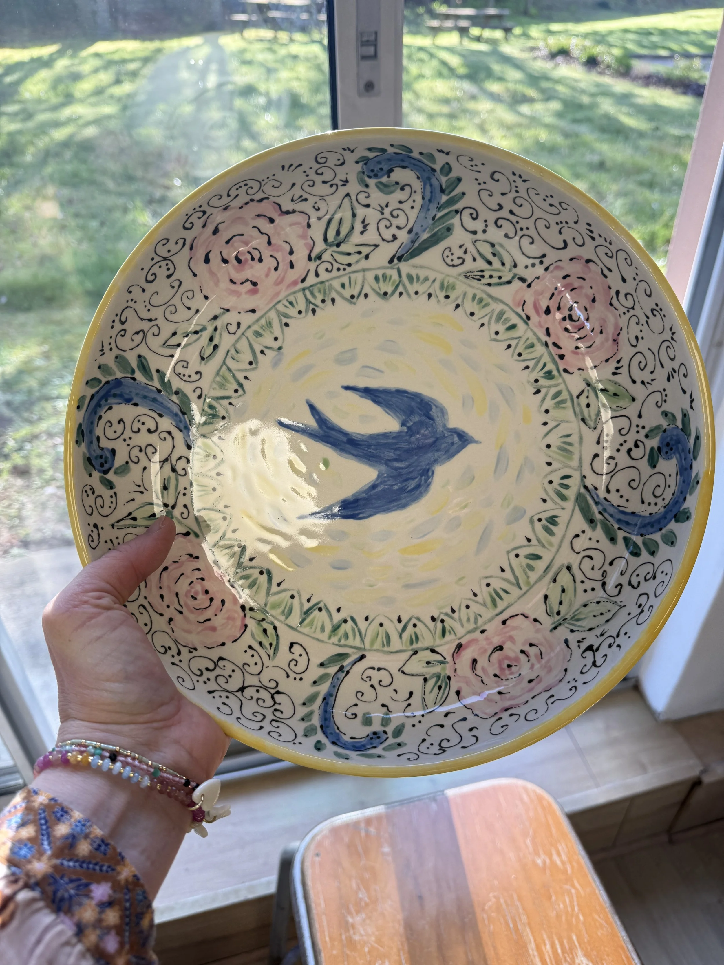 Assiette décorée avec un oiseau bleu au centre, entourée de roses roses et de motifs ornementaux.