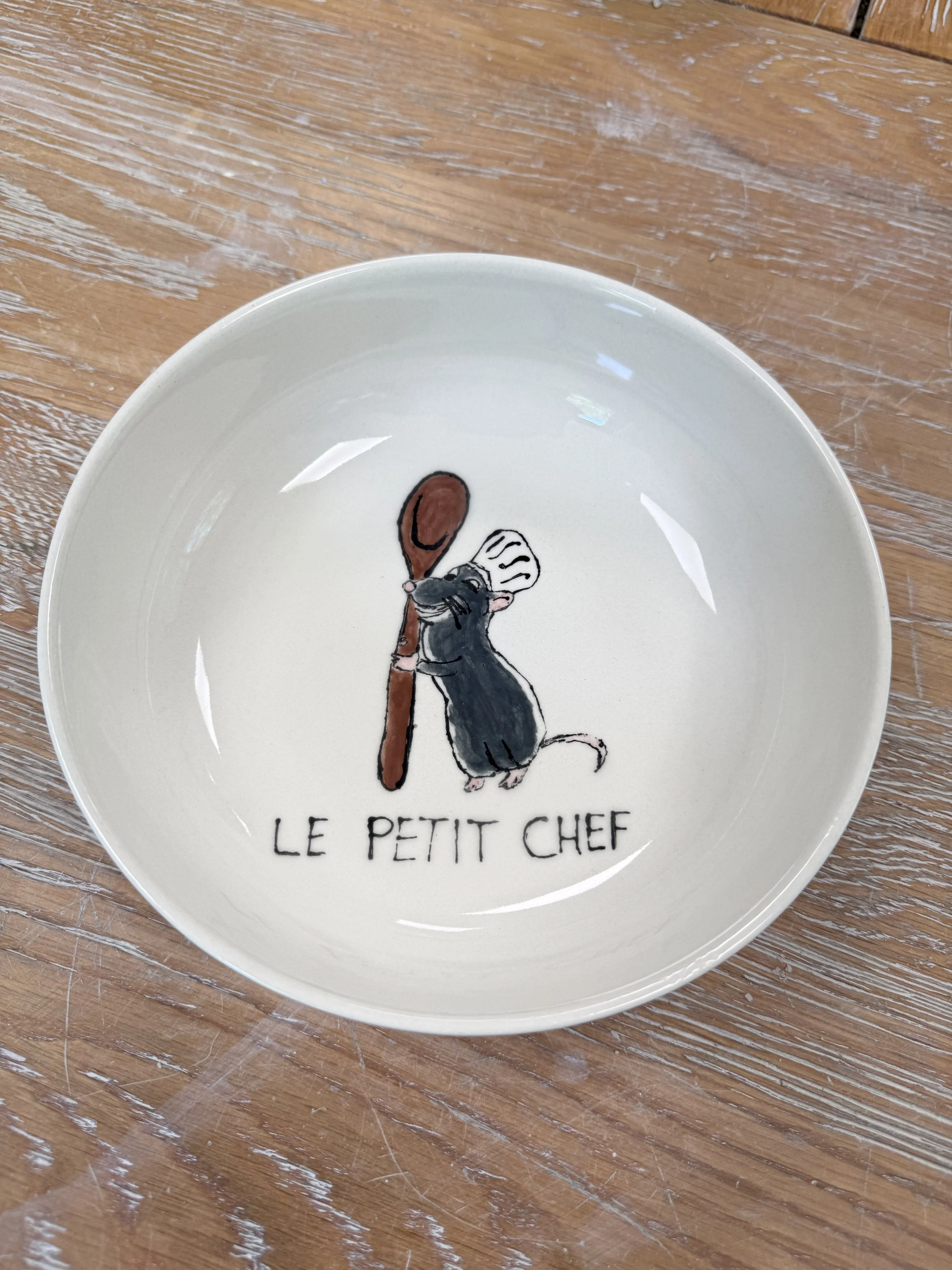 Assiette blanche avec illustration d'une souris tenant une cuillère en bois. Texte sur l'assiette : "Le Petit Chef."
