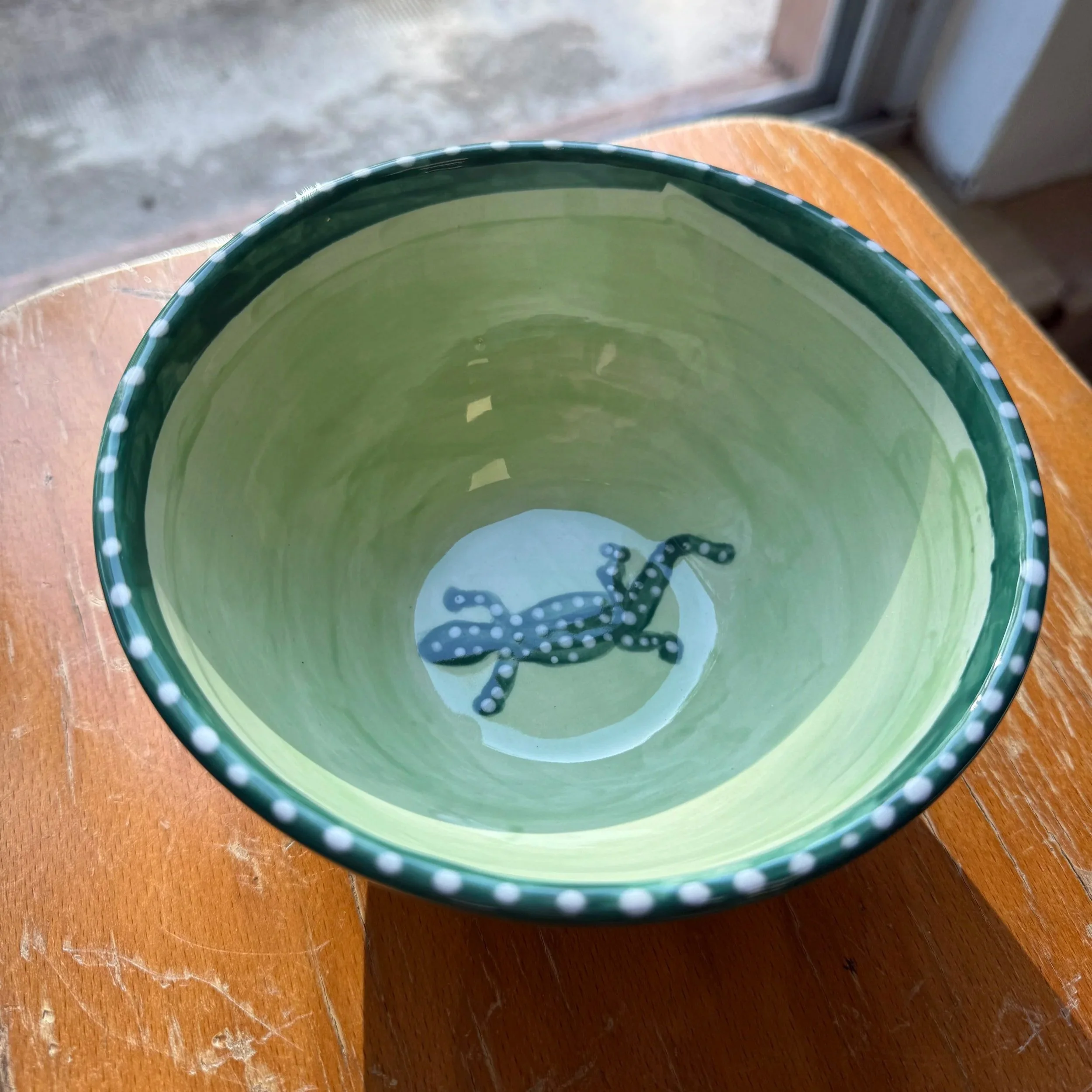 Un bol en céramique vert clair avec des pois blancs sur le bord, contenant de l'eau et une chaîne en fer Platypus dans le fond.