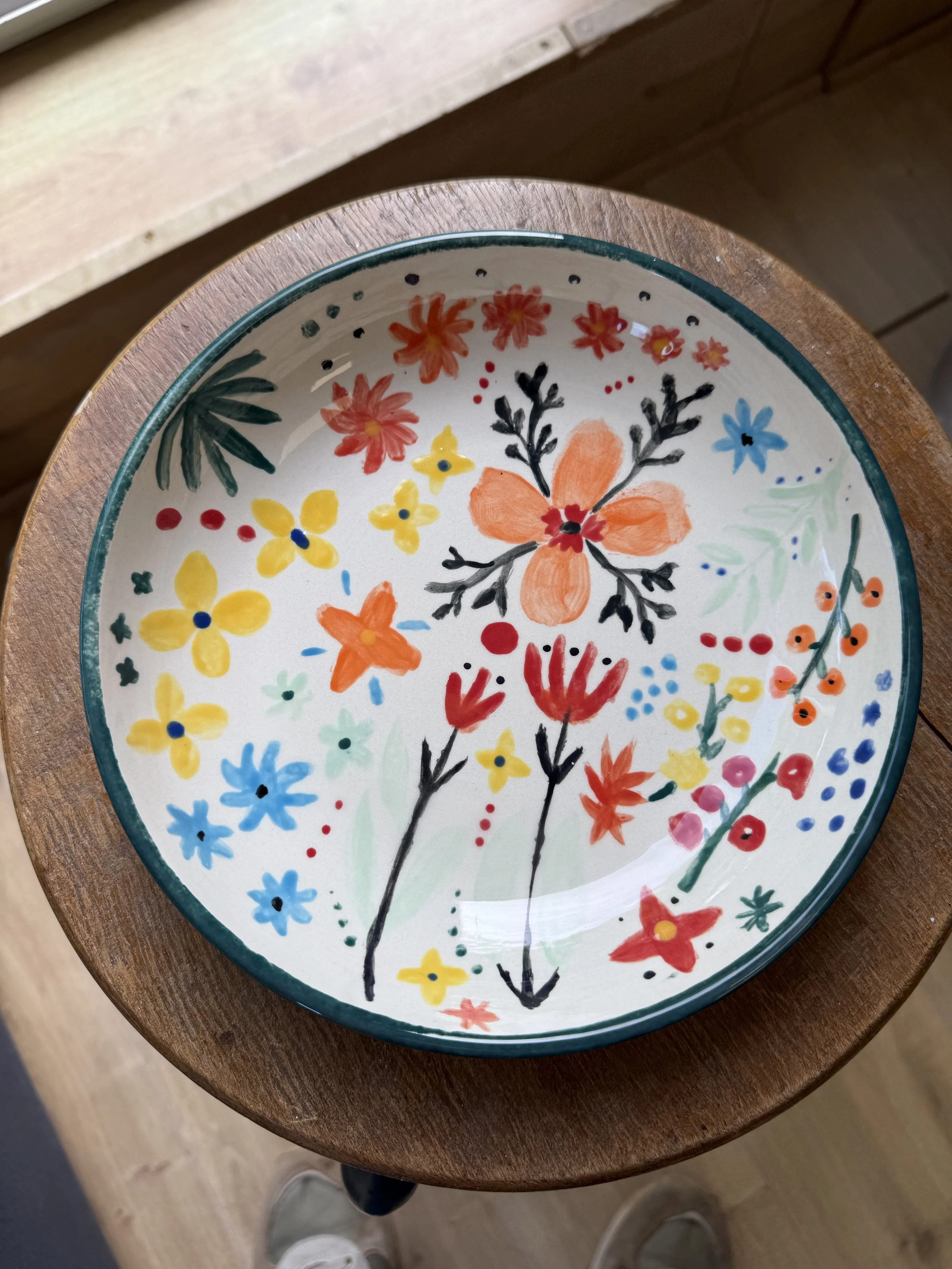 Assiette en céramique peinte à la main avec un motif floral coloré, posée sur une table en bois.