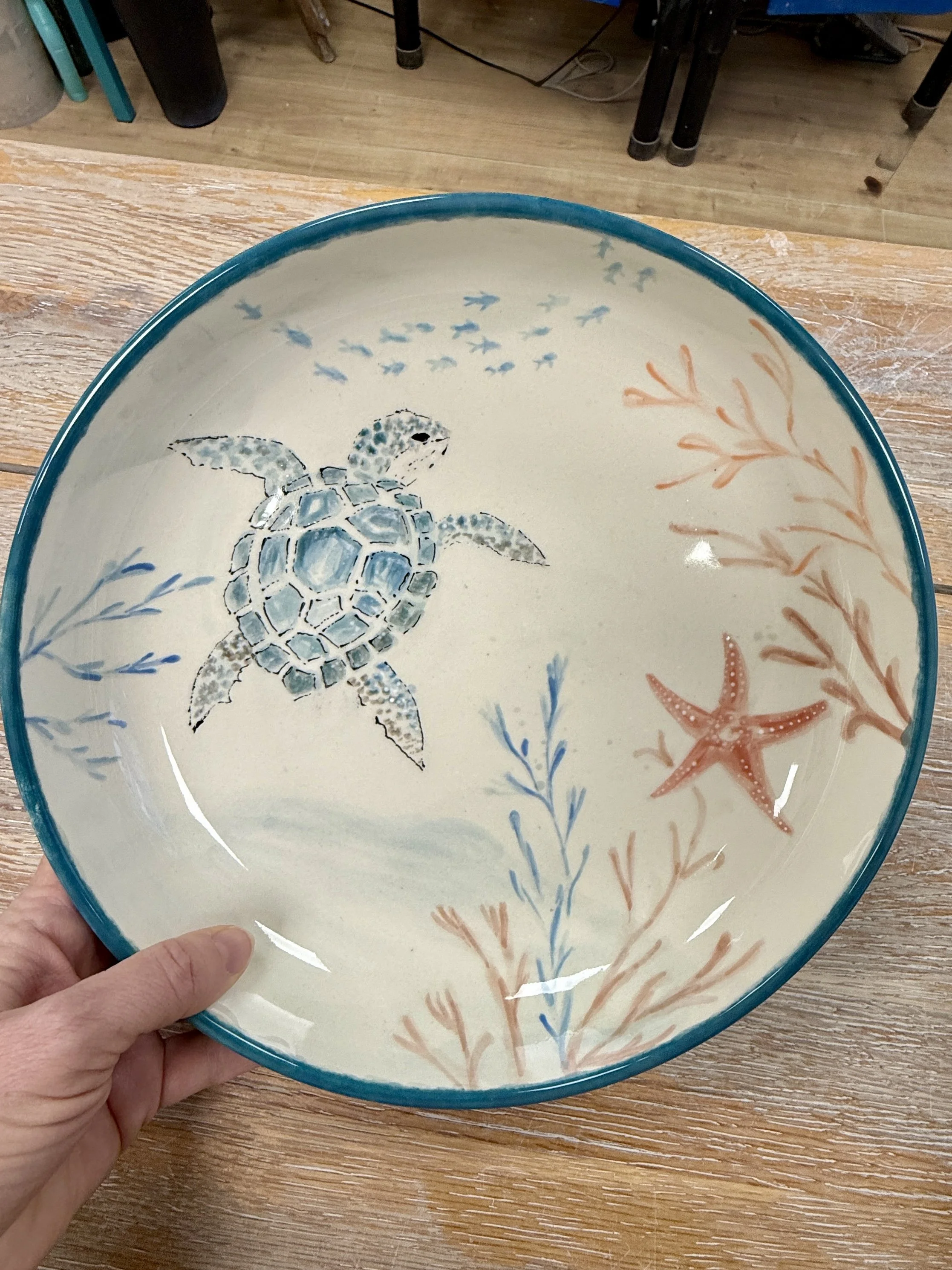 Plate décorée avec une tortue marine, une étoile de mer, des algues et des oiseaux stylisés dans des couleurs bleues, orangées et brunes.