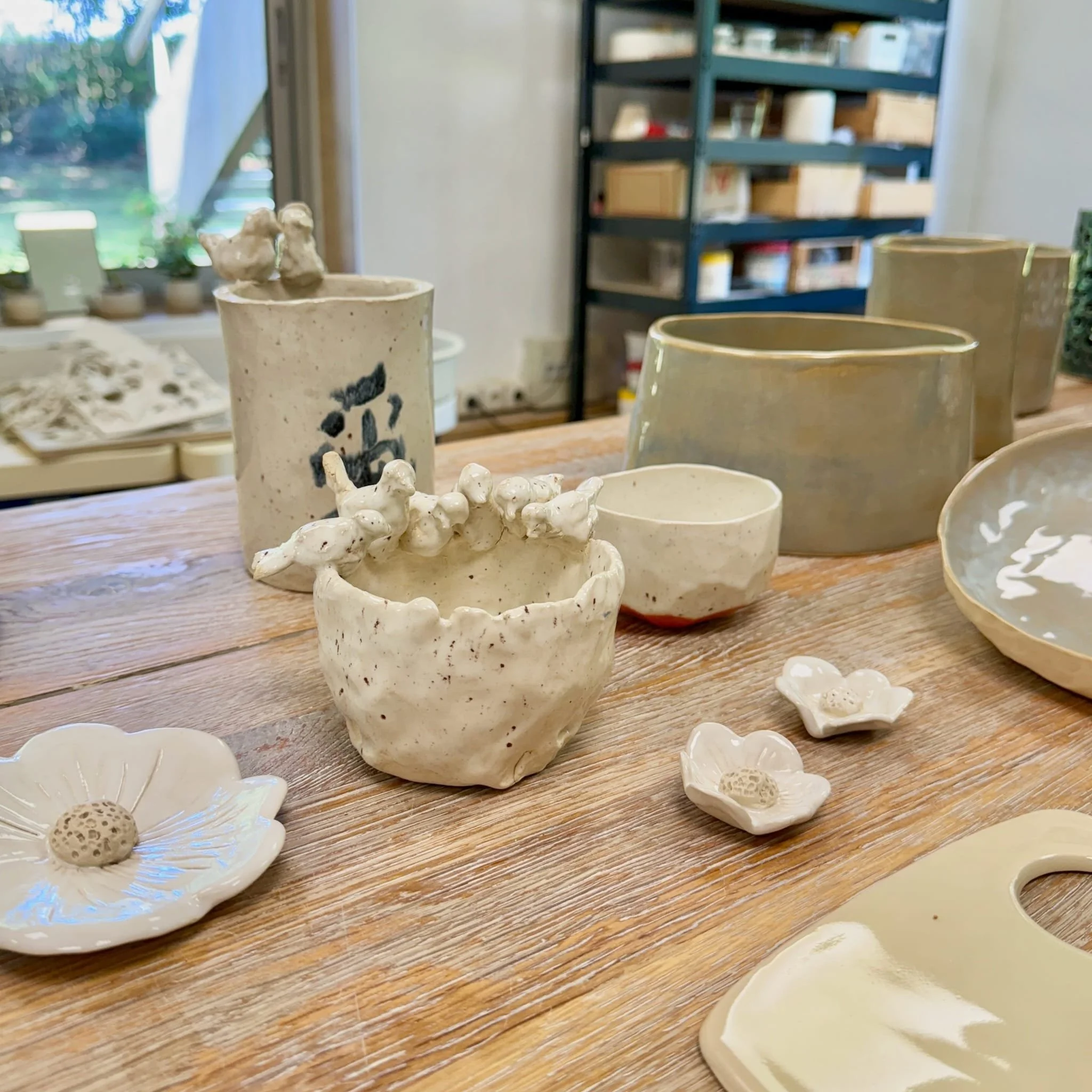 Vases et petites sculptures en céramique dans un atelier, placés sur une table en bois.