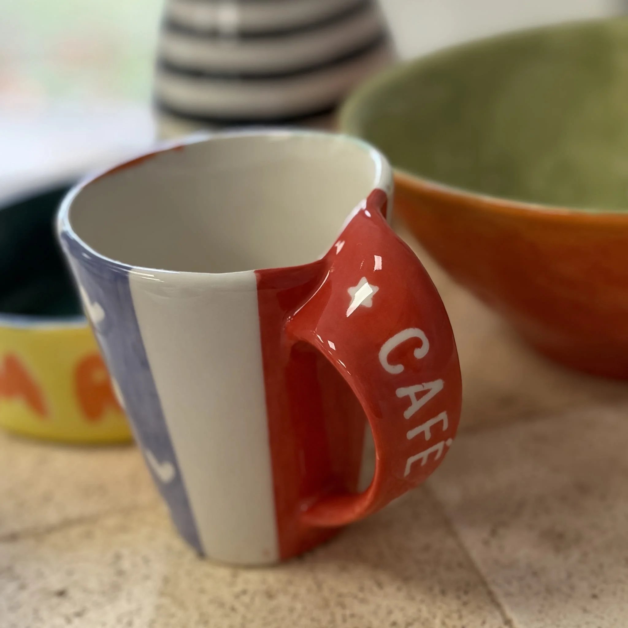 Tasse de café avec un motif aux couleurs françaises, et deux autres bols aux motifs colorés en arrière-plan.