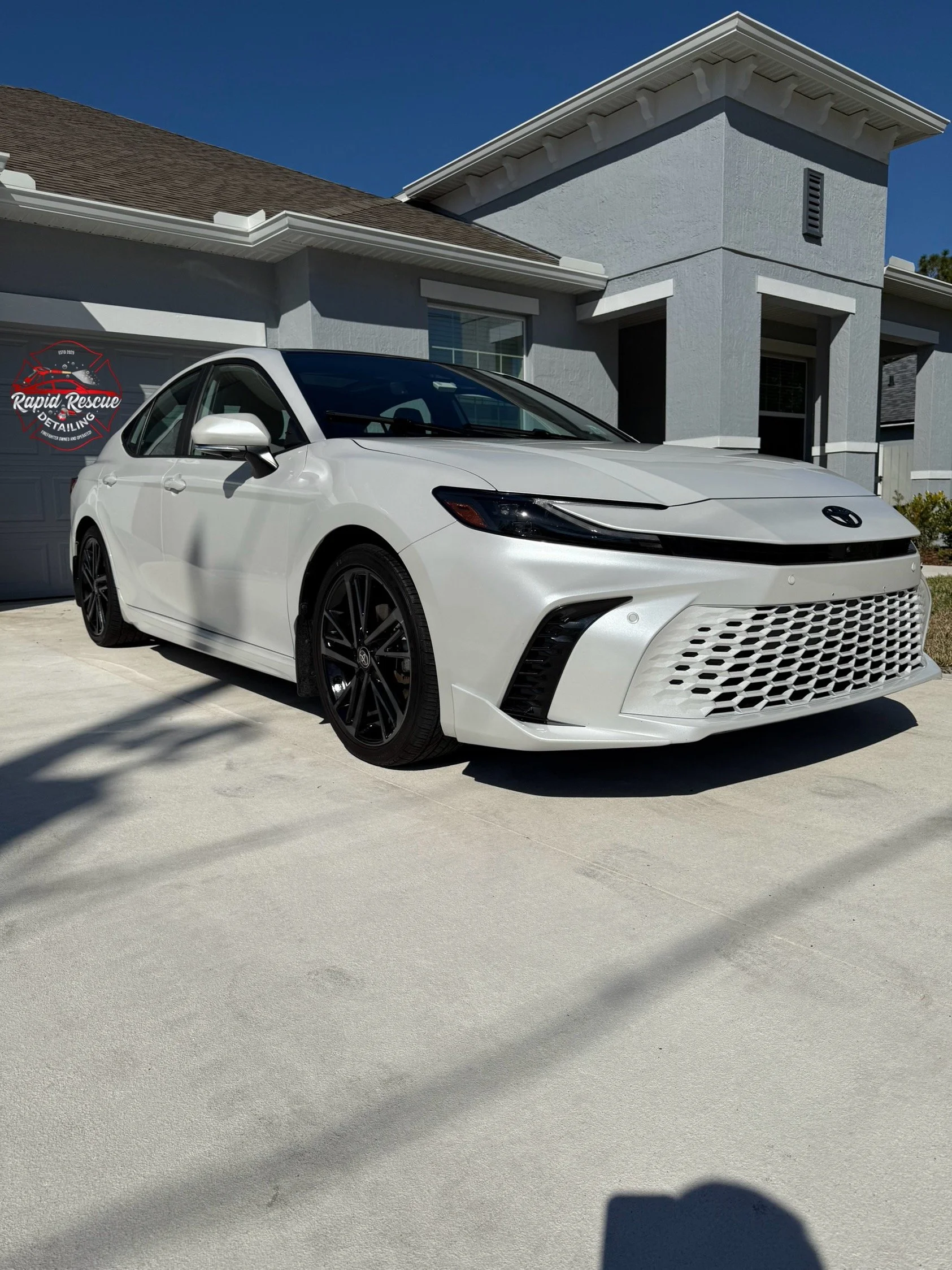 White sedan car parked in front of a modern house under a blue sky.