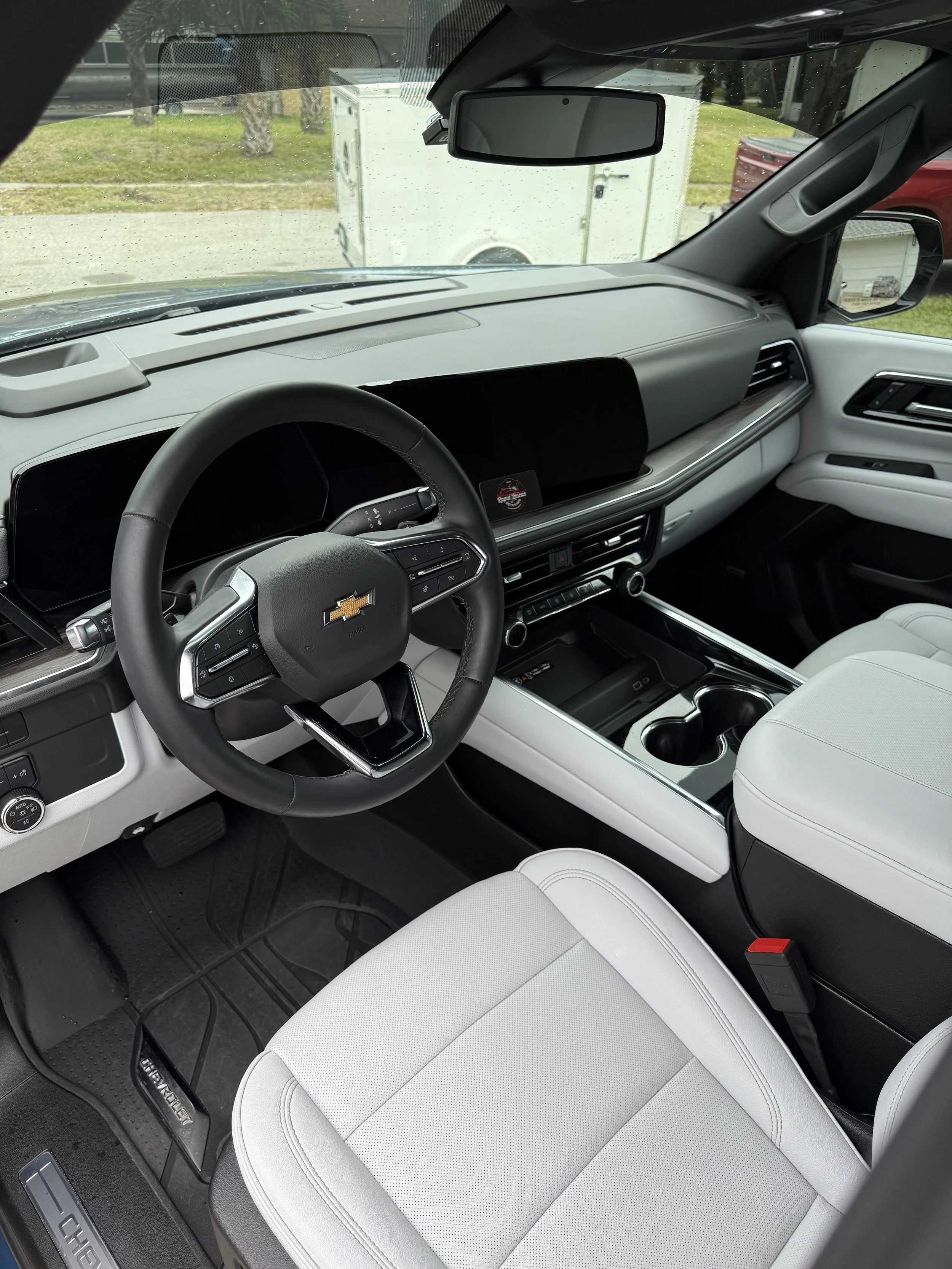 Interior of a Chevrolet vehicle showing a steering wheel, digital dashboard, gear shift, and white seats with cup holders.