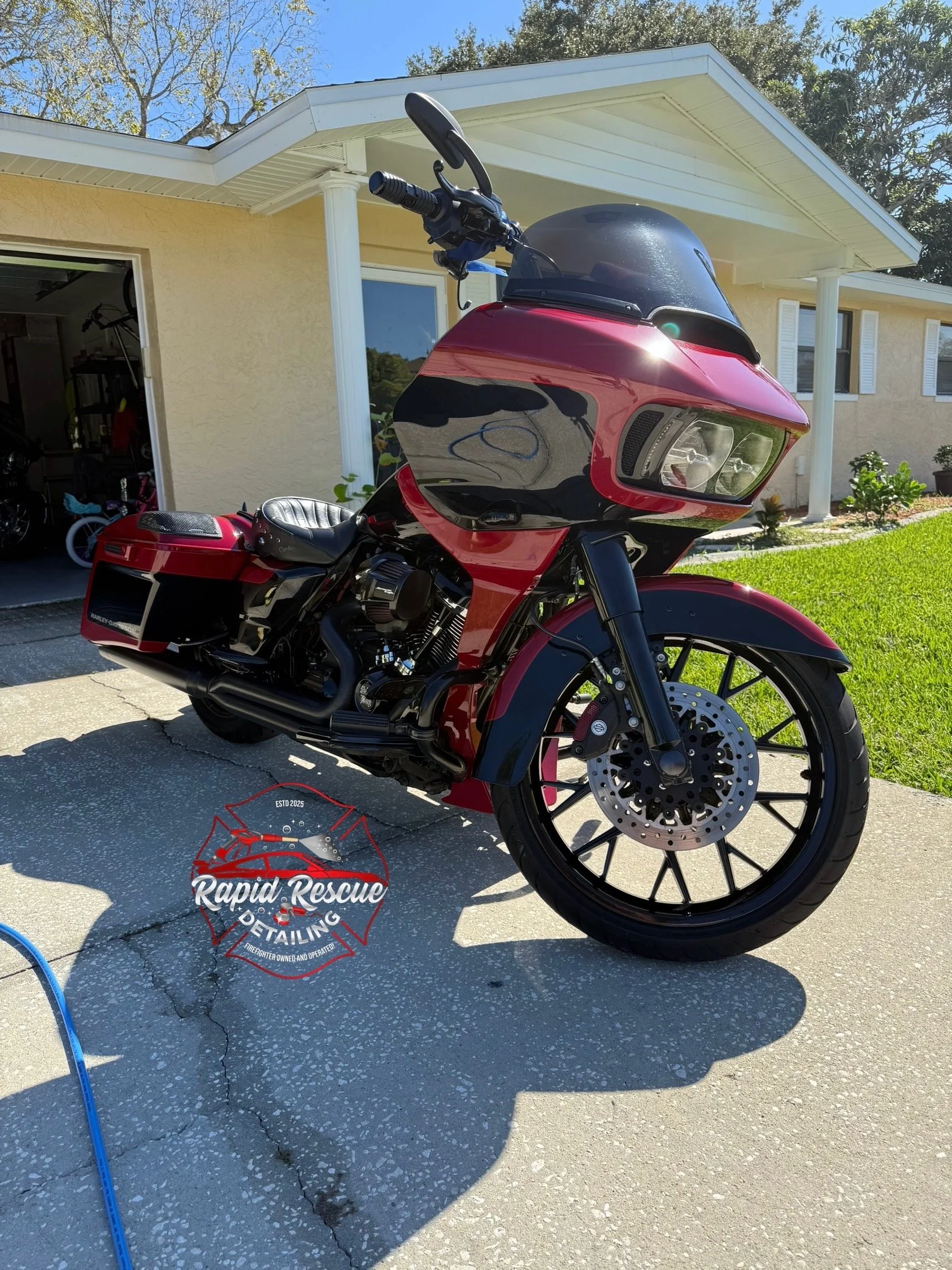 Red and black motorcycle parked outside a house on a driveway with a grassy yard and trees in the background.