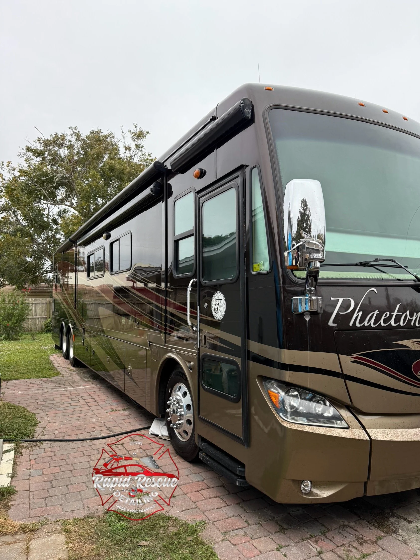 A large black and gold recreational vehicle (RV) parked on a brick driveway with a tree and fence in the background.