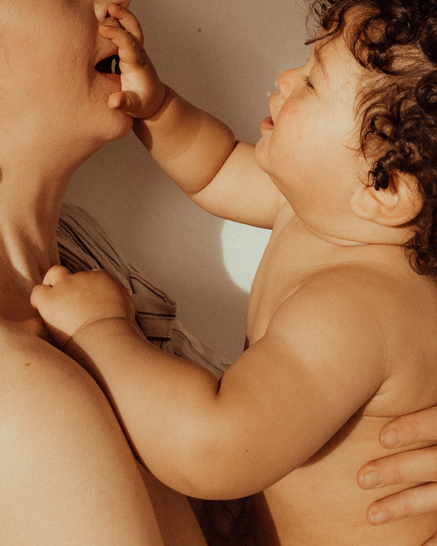 A young child with curly hair gently touching the lips of a woman, possibly a parent, in an intimate moment.