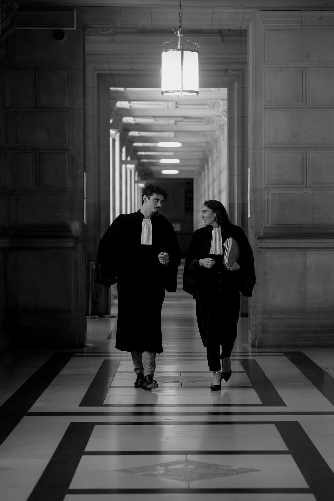 Deux avocats marchent côte à côte dans la salle des pas perdus de la Cour d'appel de Paris, d'un Tribunal ou d'un Palais de justice. Avocats en noir et blanc.