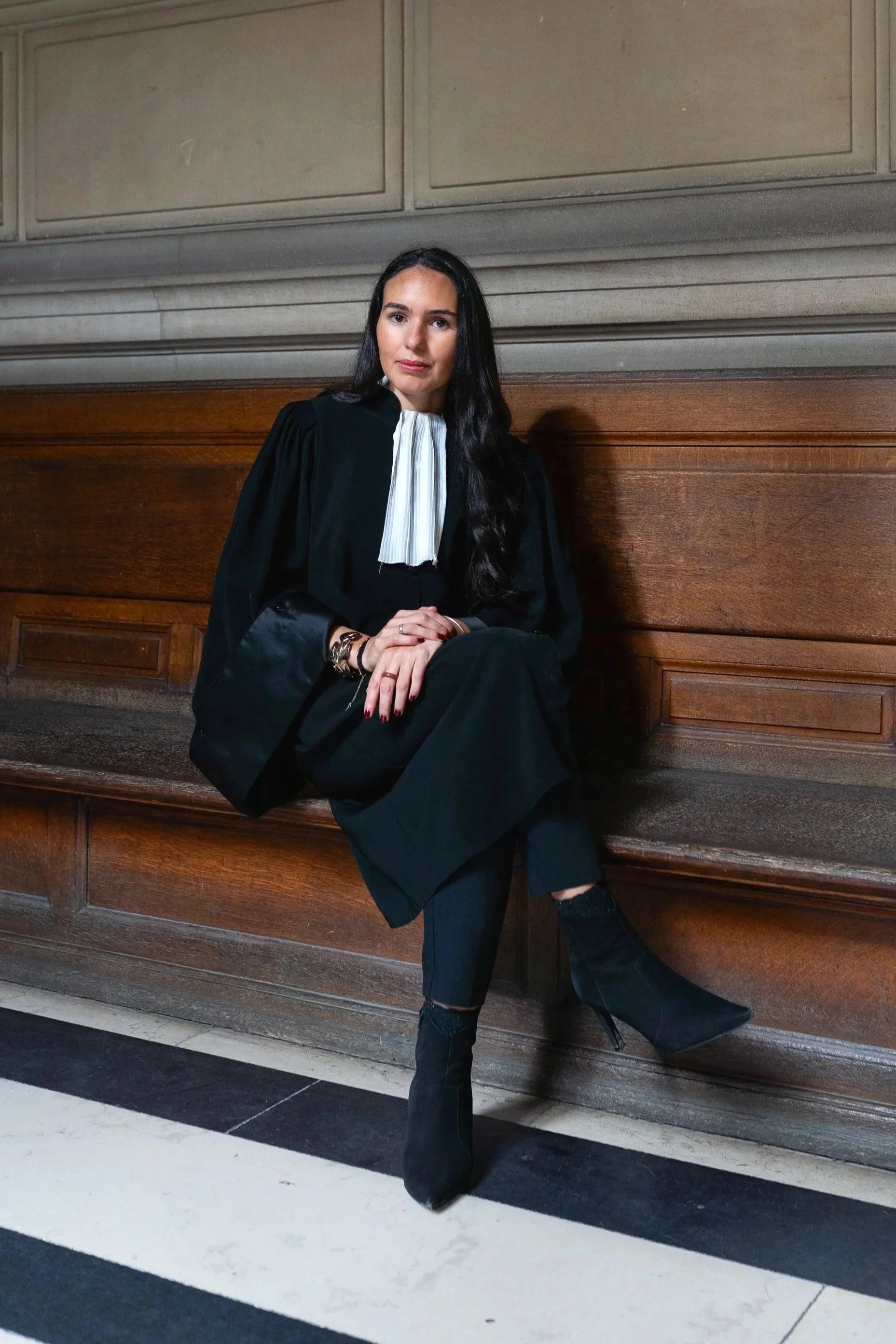 Avocates en robe noire et talons assise sur un banc en bois dans un palais de justice.