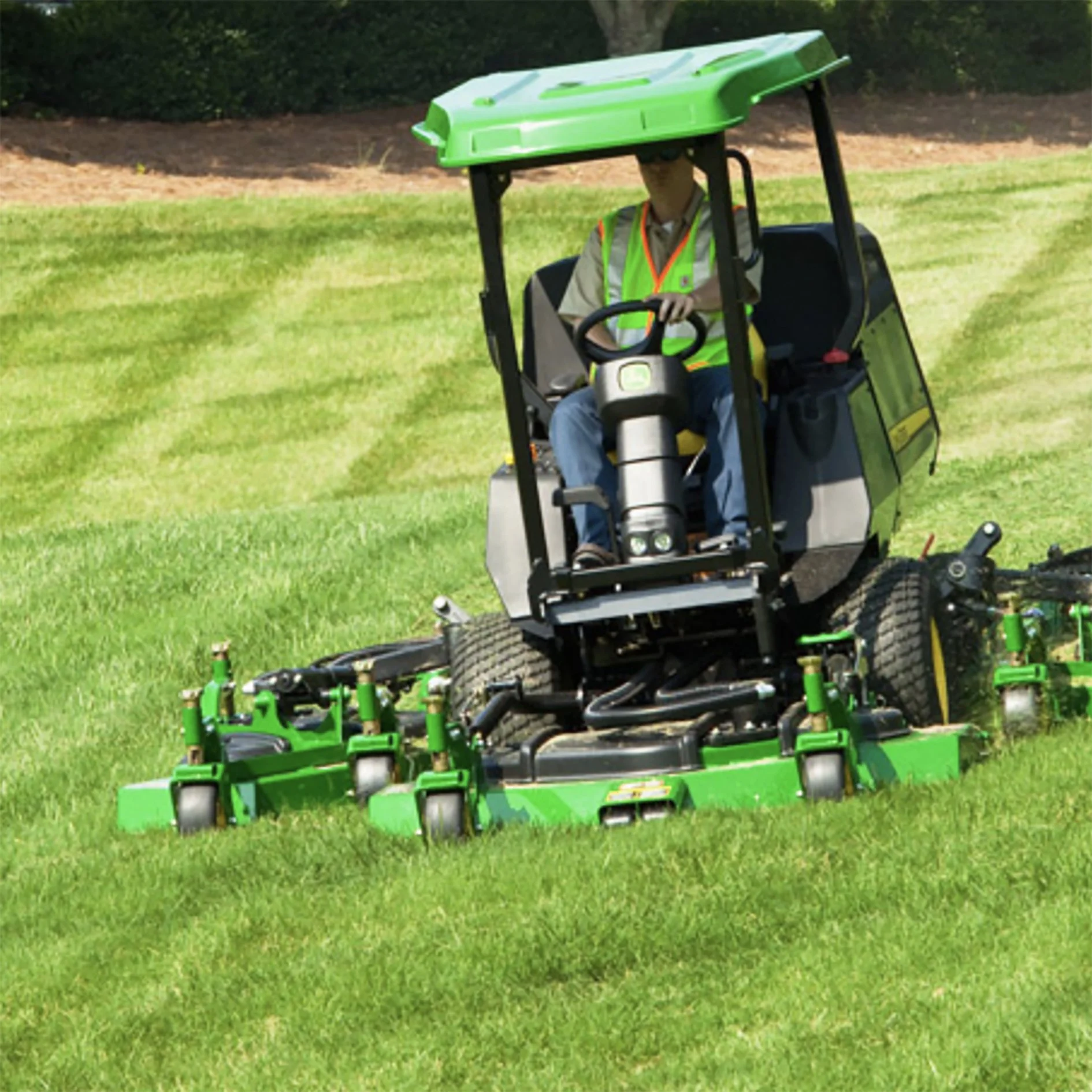 A person operating a green riding lawn mower on a grass field.