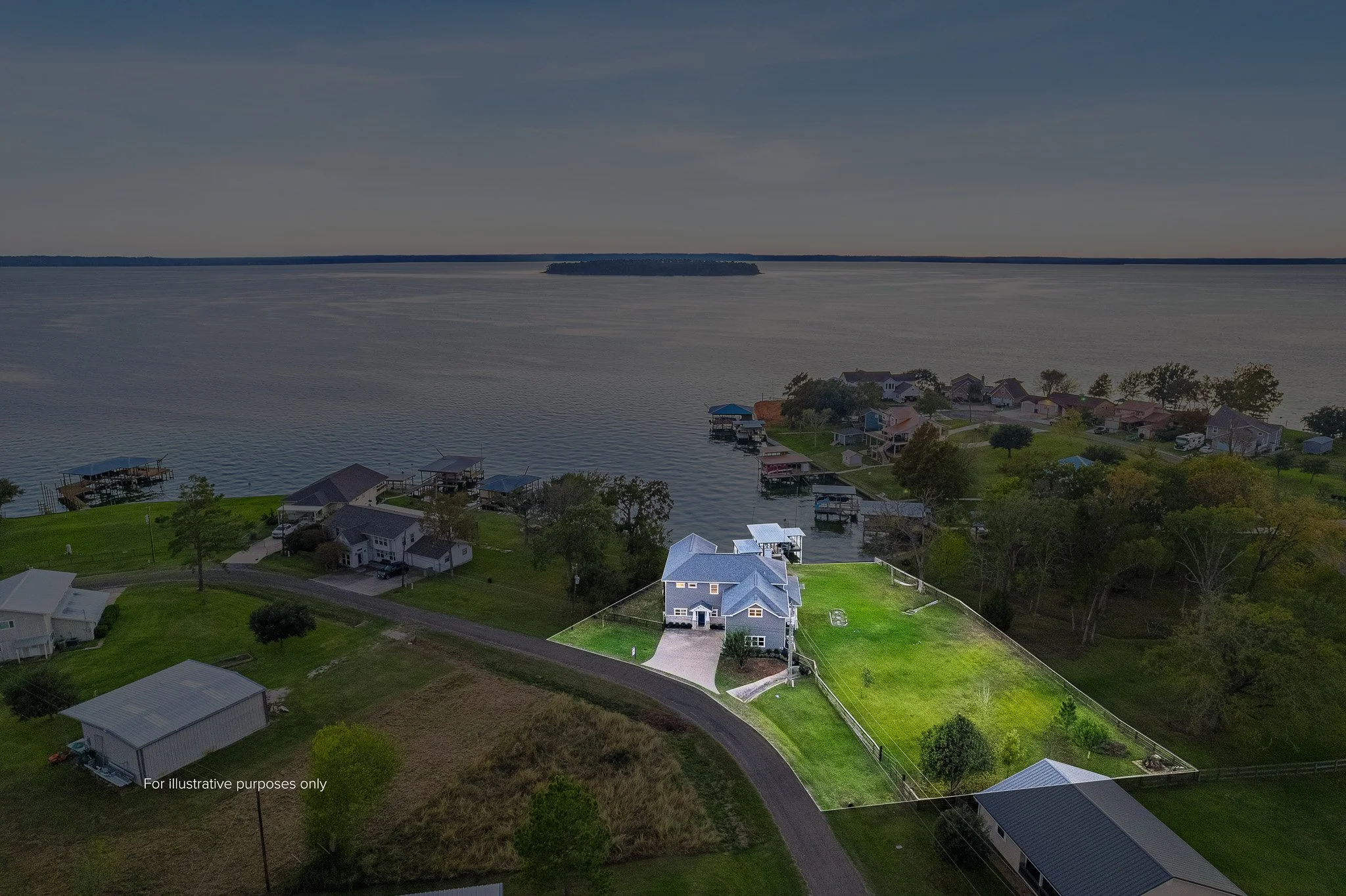 Aerial view of a house with a blue roof on a green lawn next to a body of water, with neighboring houses and boat docks along the shoreline.