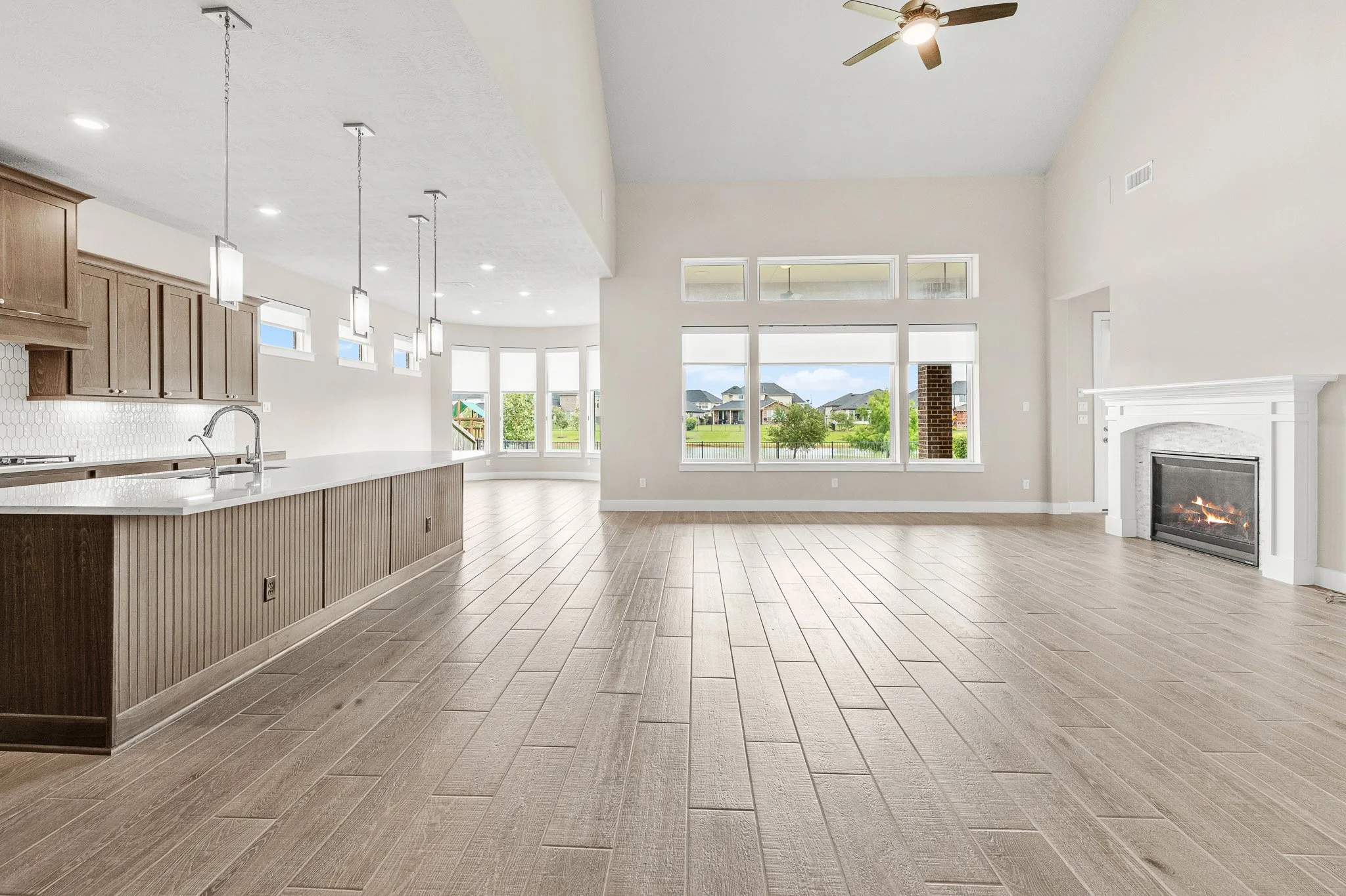 Empty open-concept living room and kitchen with large windows, hardwood floors, a fireplace, and ceiling fan.
