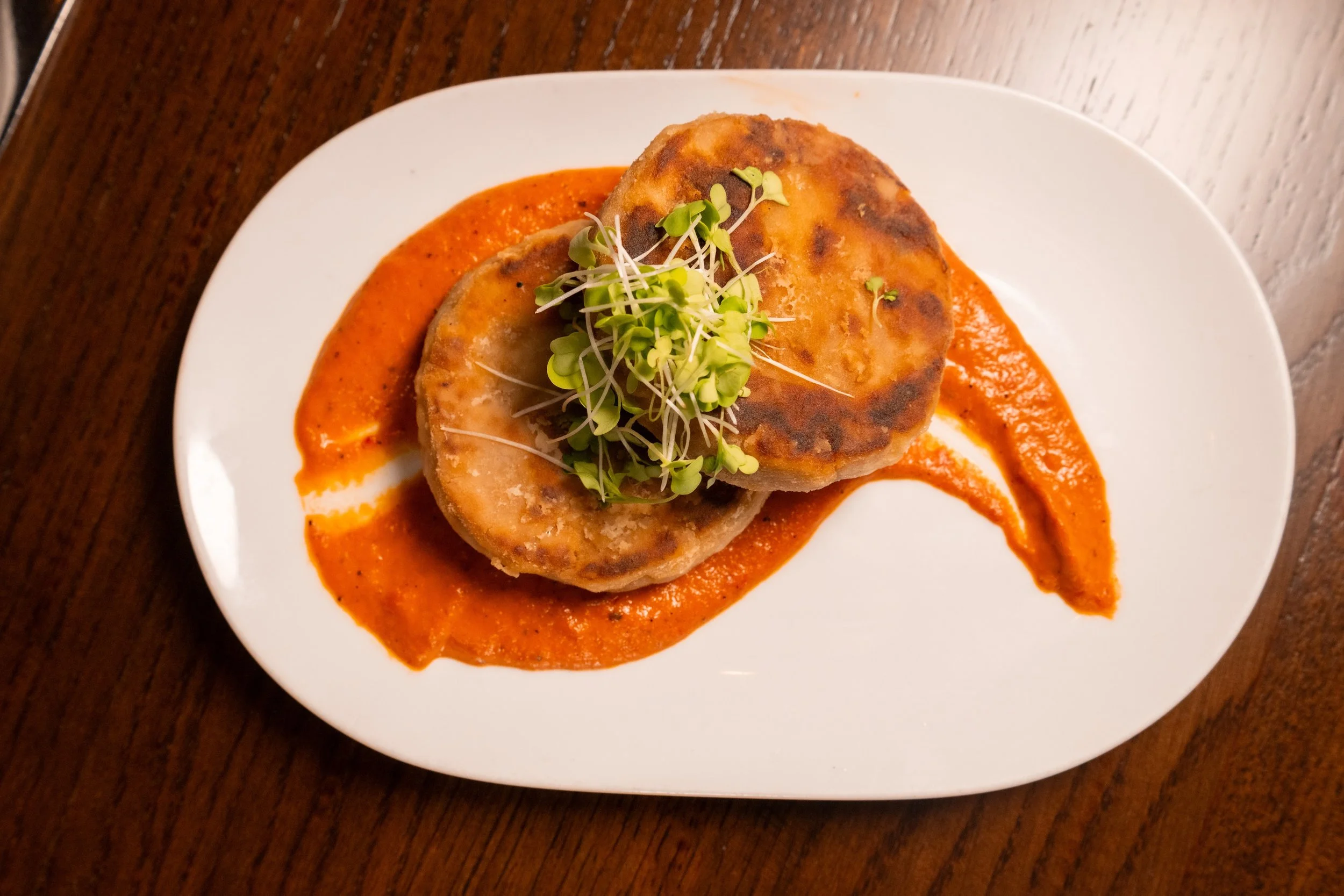 Plated Appetizer at The Hemingway Steakhouse featuring crab cakes with microgreens and red pepper sauce.
