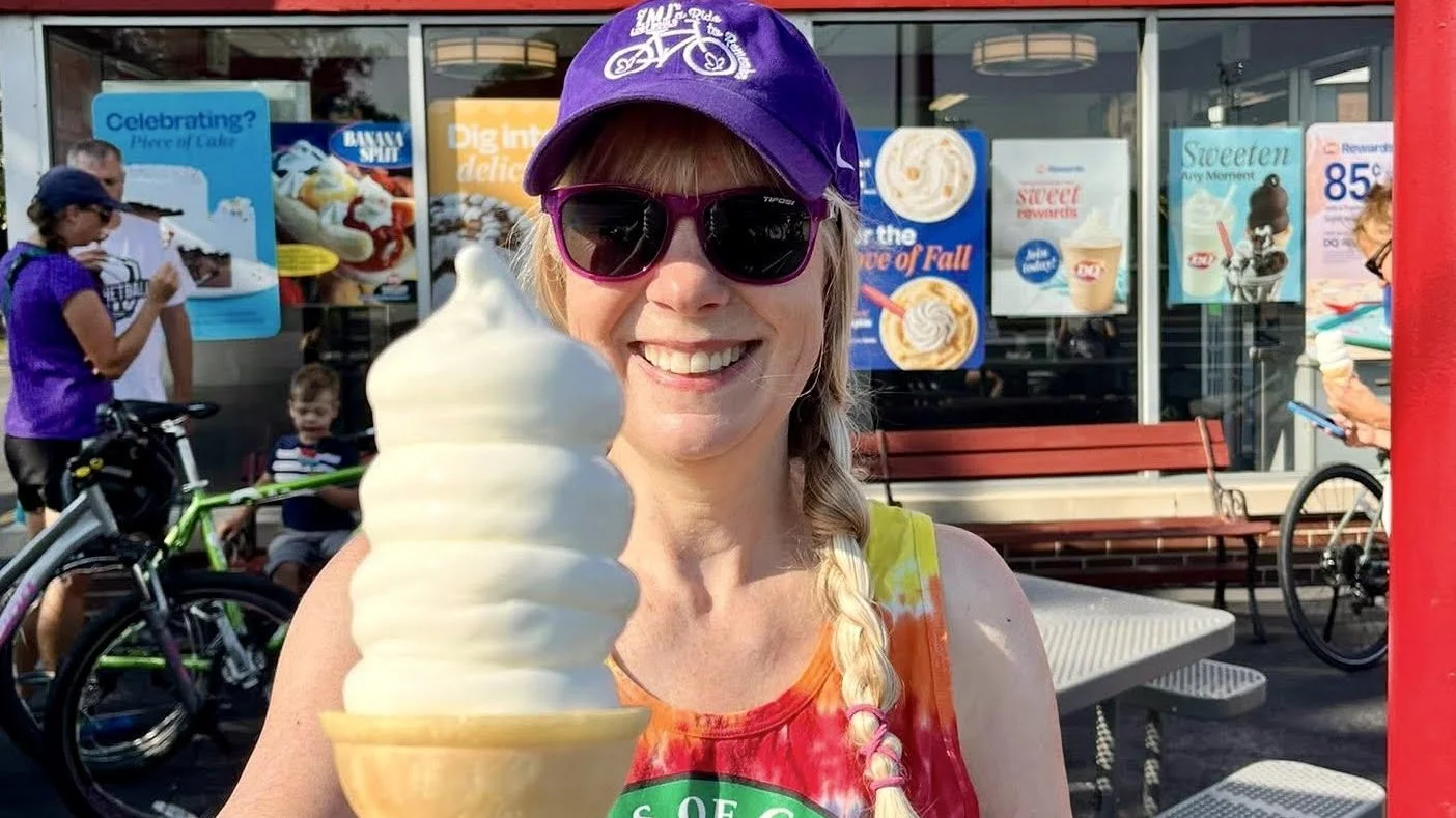 Woman smiling in the sunlight holding up an ice cream cone.