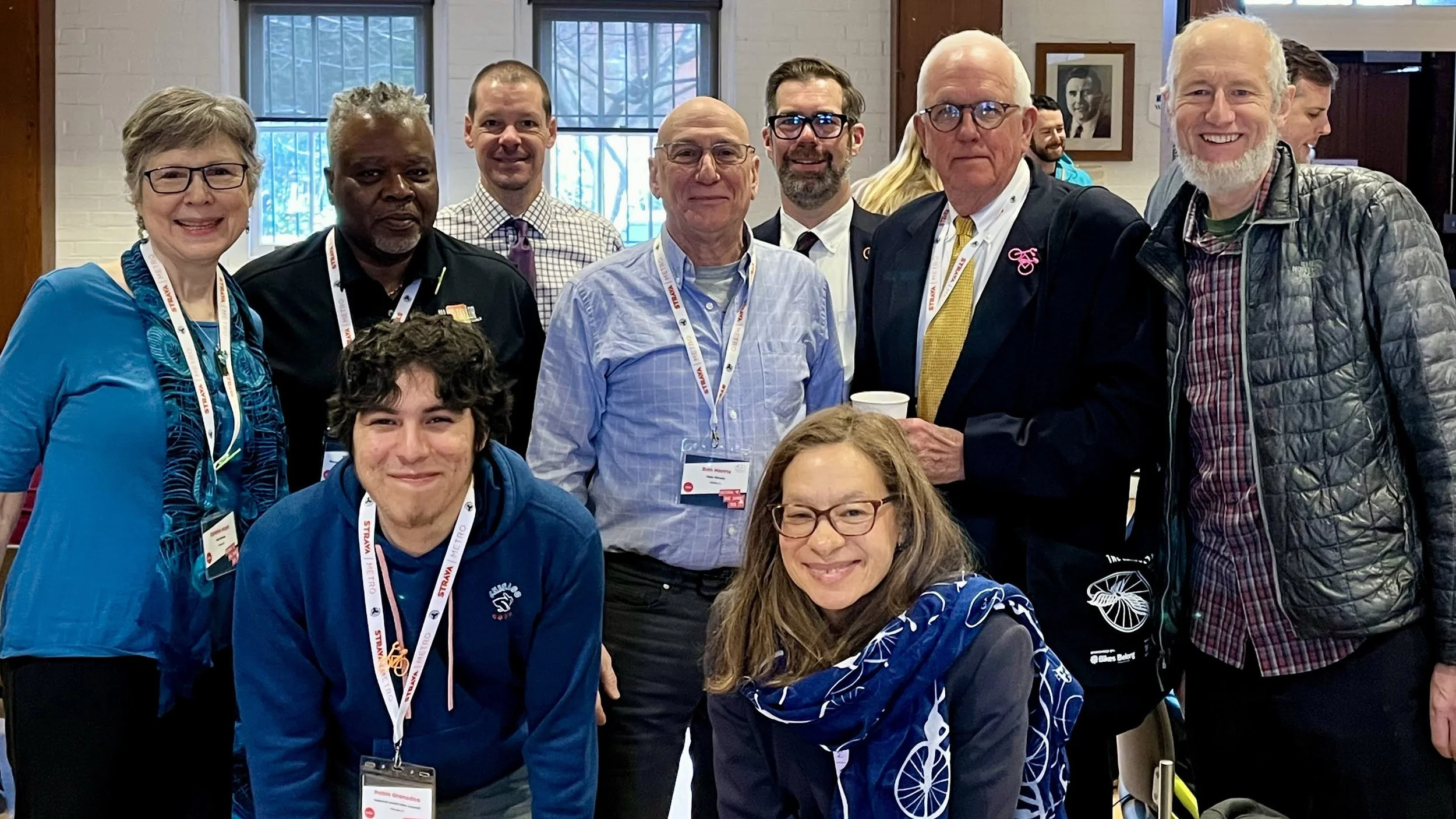 Group of diverse people smiling and posing for a photo indoors at a conference or event, with name badges around their necks.